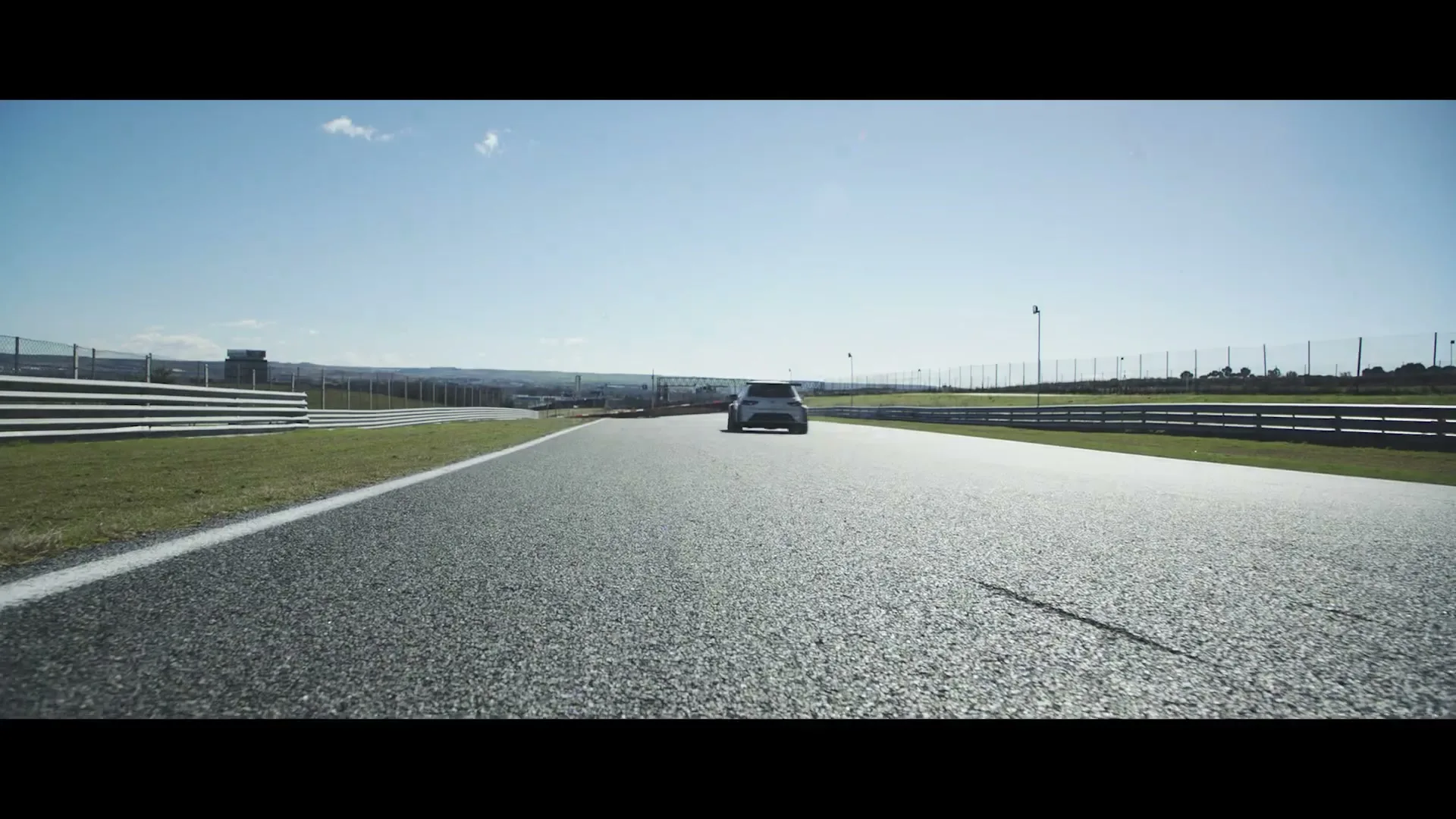 A white race car with colorful accents drives quickly around a track on a sunny day, with a clear blue sky overhead.