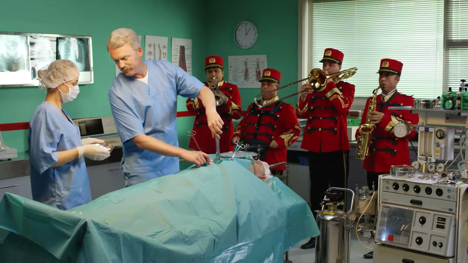 A male surgeon operates on a patient while a female nurse assists, and a brass band in red uniforms plays in the background of a hospital operating room.