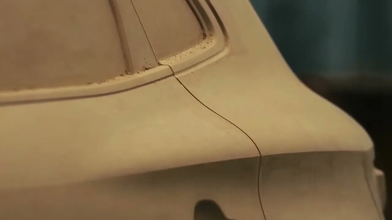 A close-up shot of a clay model of a car's rear quarter panel, showing intricate design lines and curves in a workshop.