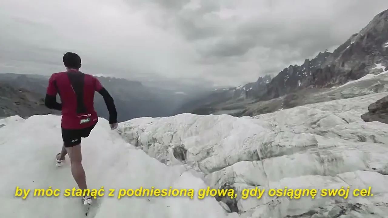 A male runner in a red shirt and black shorts runs across a vast, icy glacier with mountains in the background under a cloudy sky.