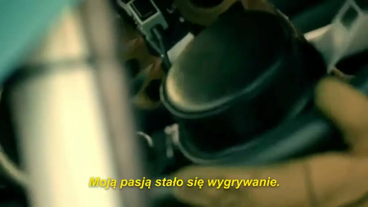 A person in racing gloves adjusts a car's steering wheel, with a yellow subtitle visible at the bottom of the screen.