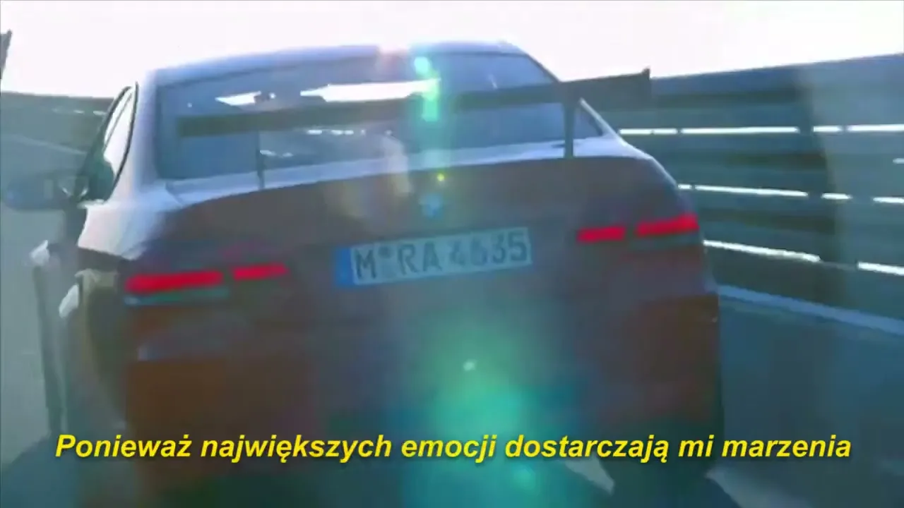 A red BMW sports car with a spoiler drives away on a sunny day, with a lens flare visible.