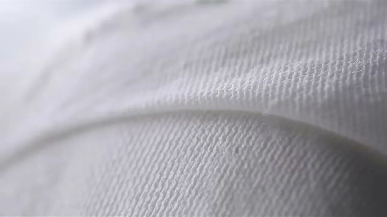 A macro shot of white fabric with a textured weave, showing subtle movement and folds, in a bright, clean setting.