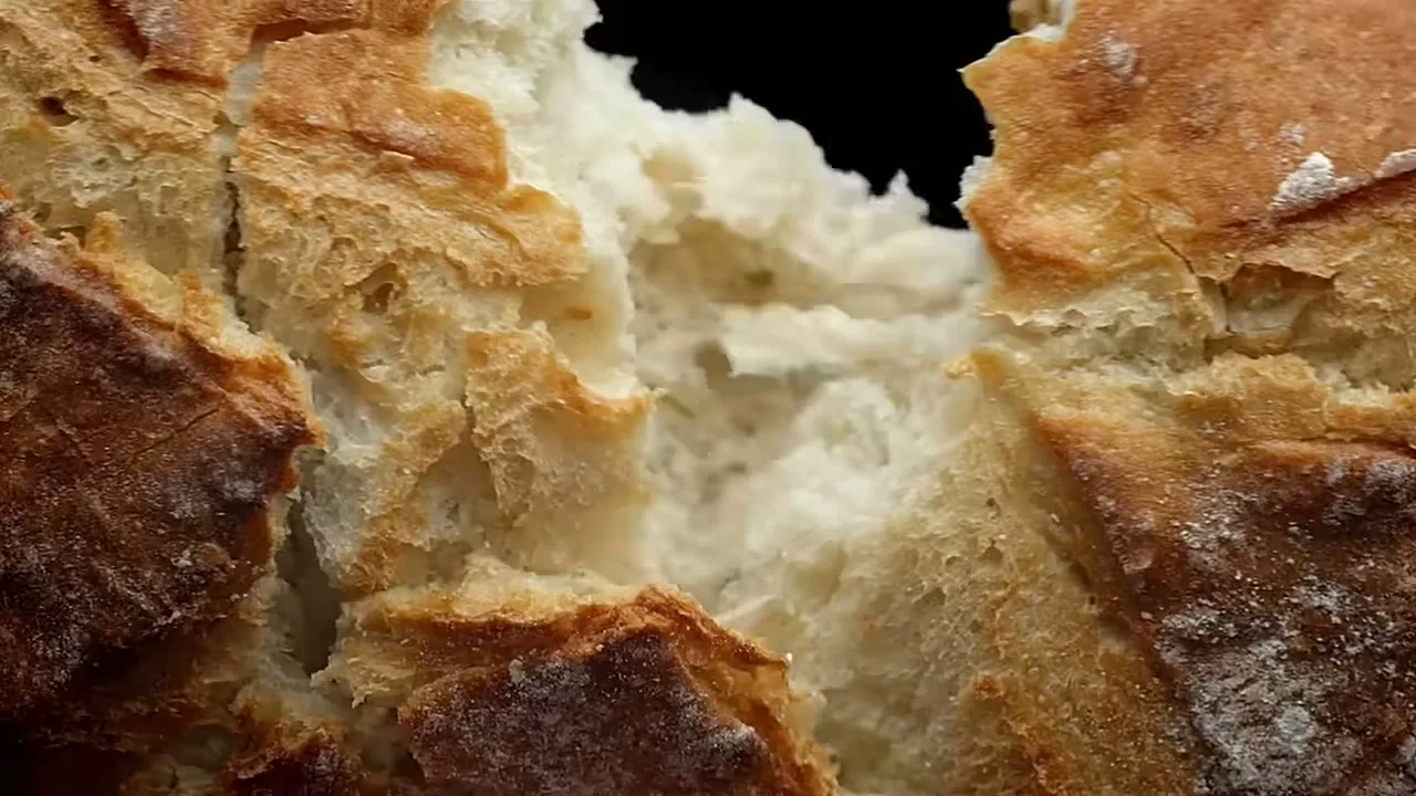 A close-up shot shows a loaf of bread being torn apart, revealing its soft white interior and crusty golden-brown exterior.