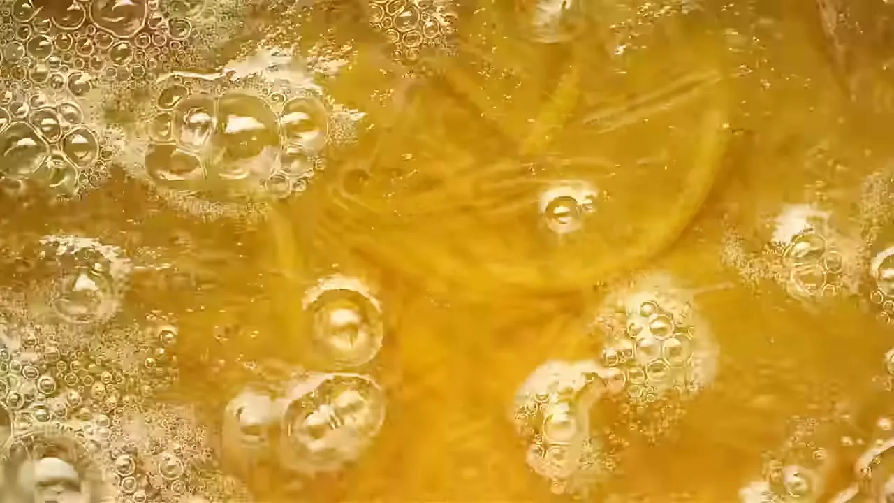 A close-up shot shows orange slices and bubbles in a golden liquid, as if boiling, with a shallow depth of field.