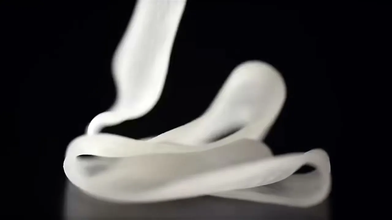 A translucent white sheet of pasta dough gracefully falls and folds onto a dark surface in a studio setting.