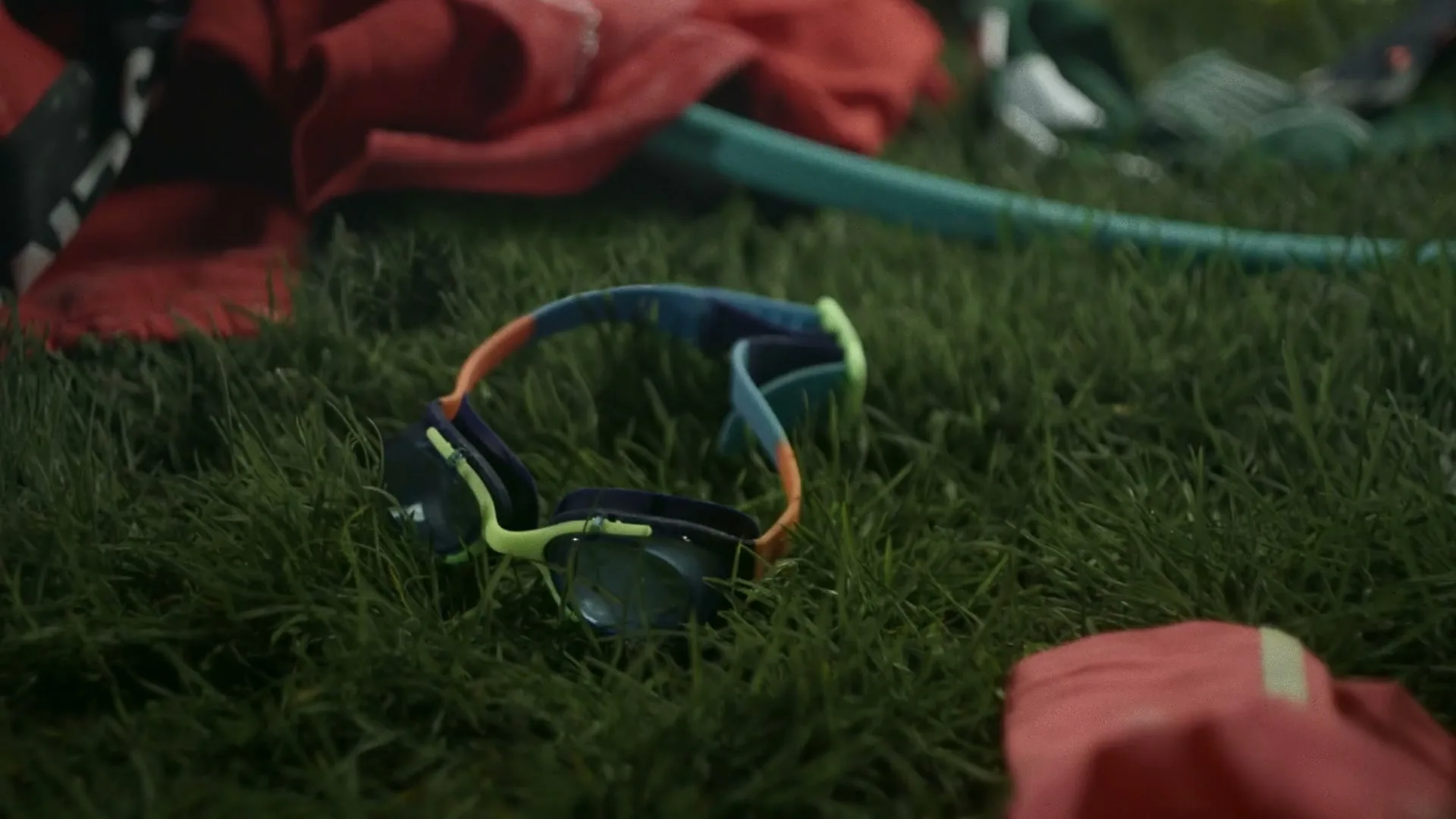 Swimming goggles lie on green grass, surrounded by other sports equipment, suggesting a break from activity.