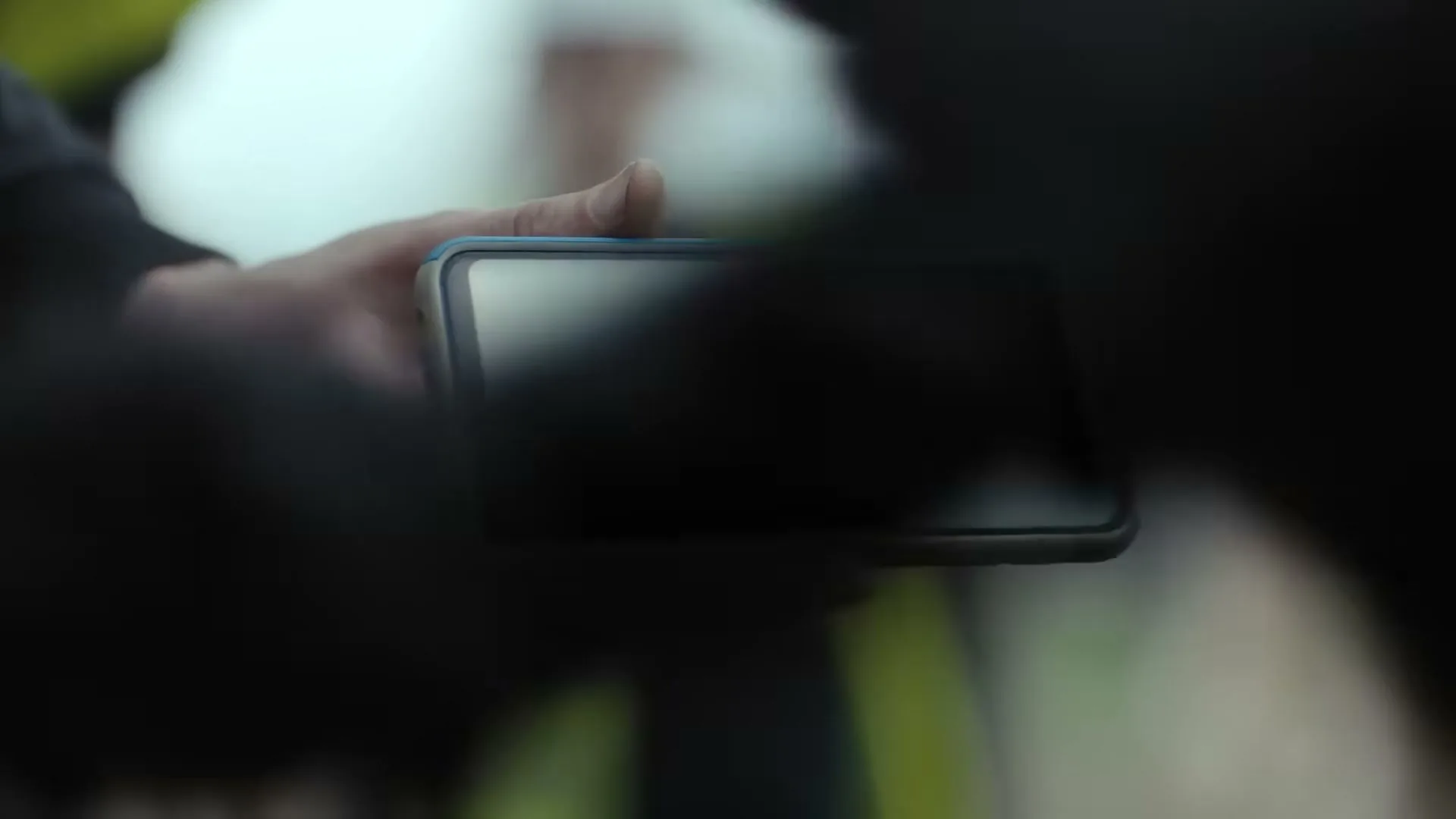 A construction worker holds a smartphone displaying the Gas Networks Ireland logo, then lowers it, revealing a blurred background of other workers.