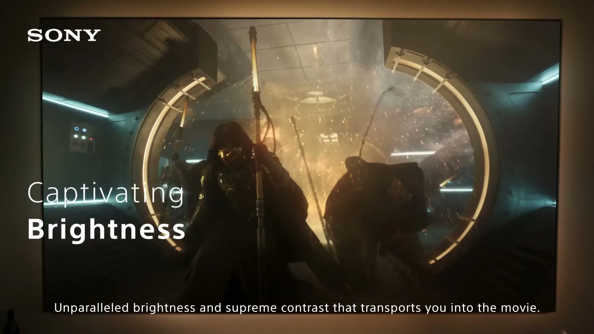 A group of armored figures with glowing staffs fight in a futuristic, circular room, displayed on a large TV screen.