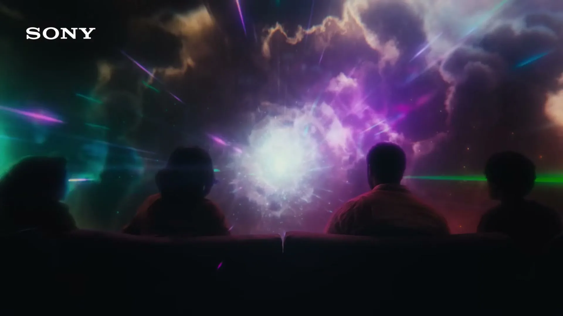 Four people sit on a couch, watching a vibrant, colorful, abstract light show on a screen, with the Sony logo visible in the top left corner.