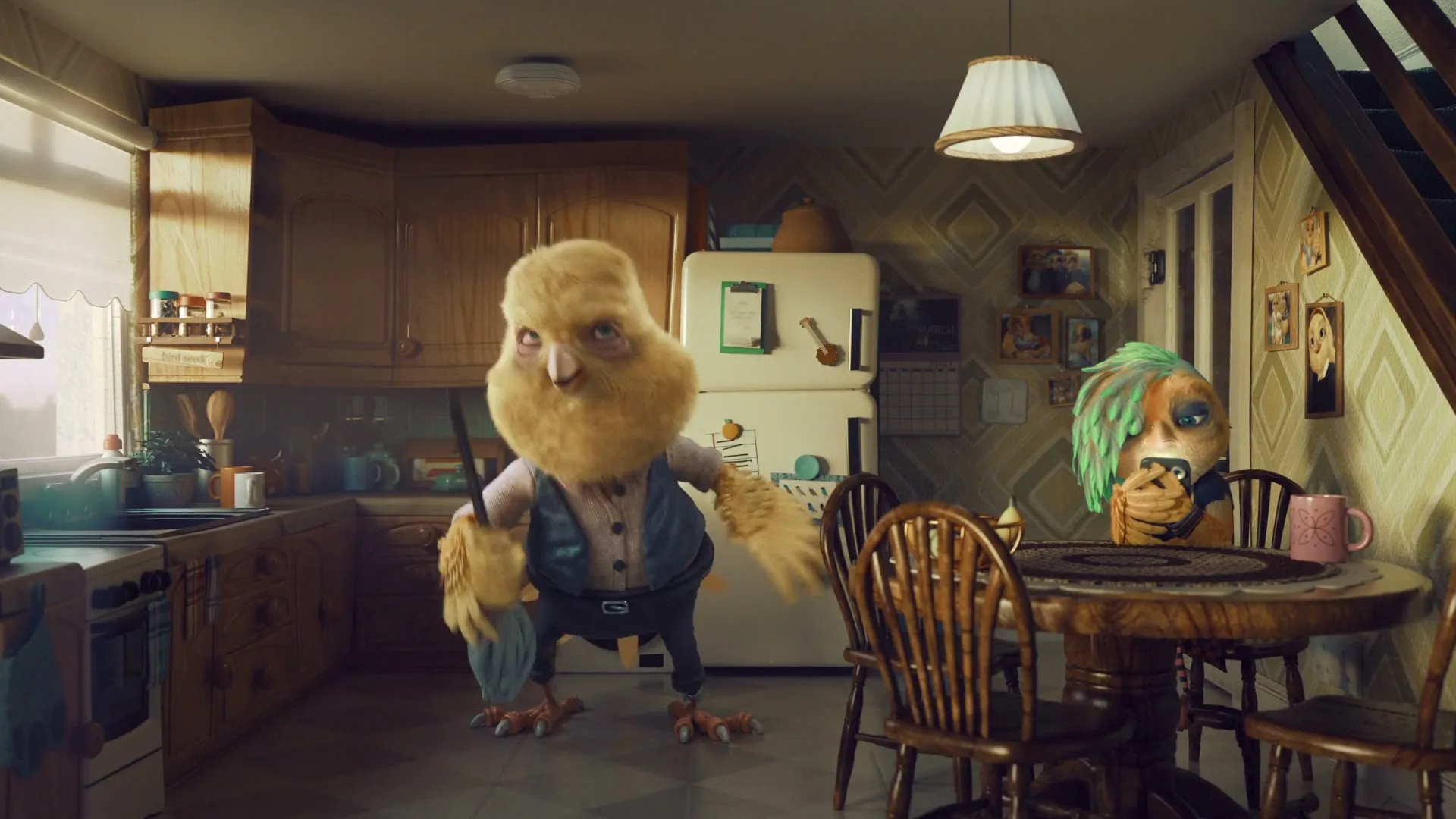 A large, fluffy, yellow bird-like creature mops the floor while a smaller, green-haired bird-like creature sits at a table, looking at a phone in a kitchen.