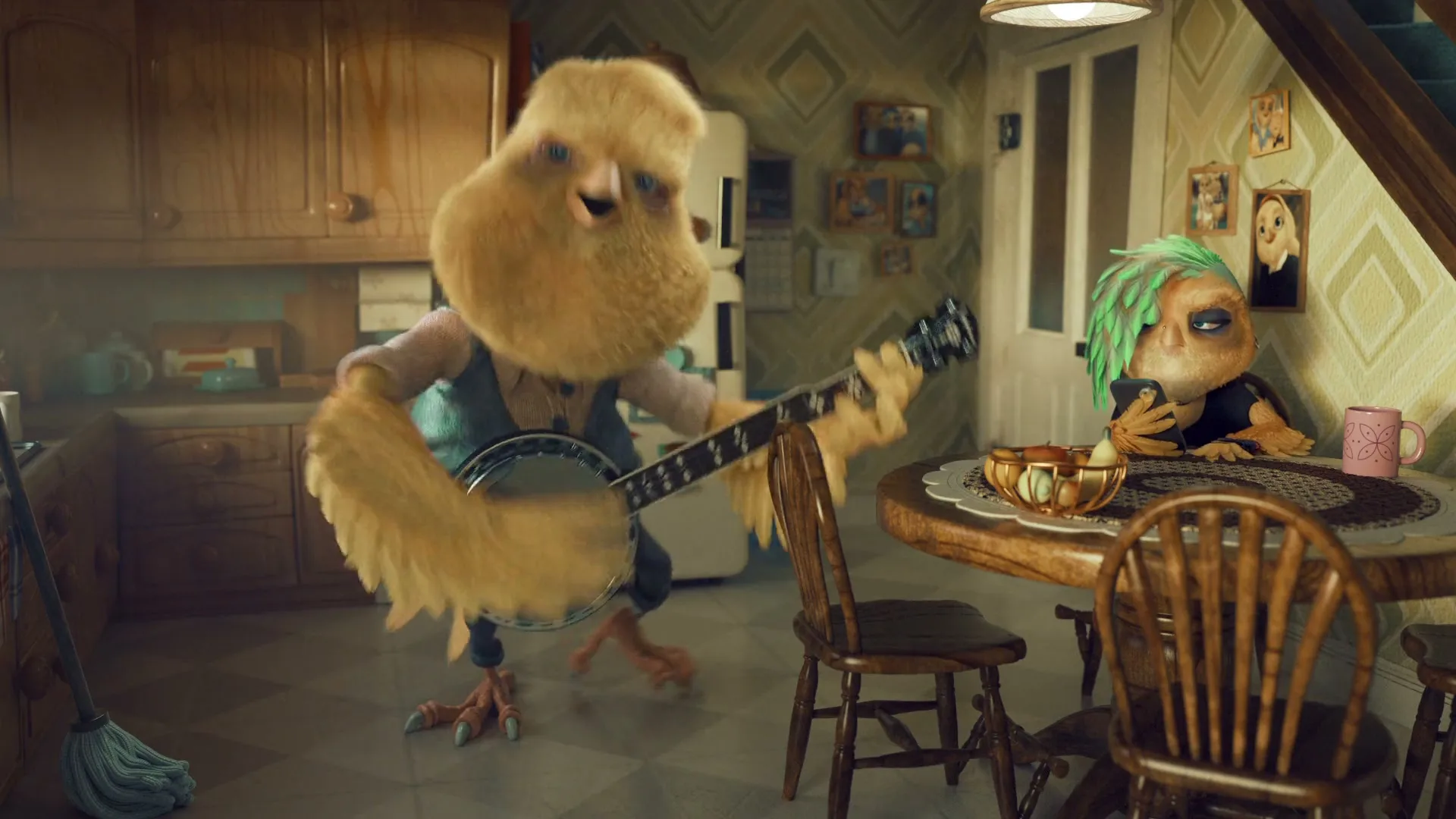 A fluffy, yellow, bird-like creature with a beard plays a banjo in a kitchen while another bird-like creature with green hair sits at a table, looking annoyed.