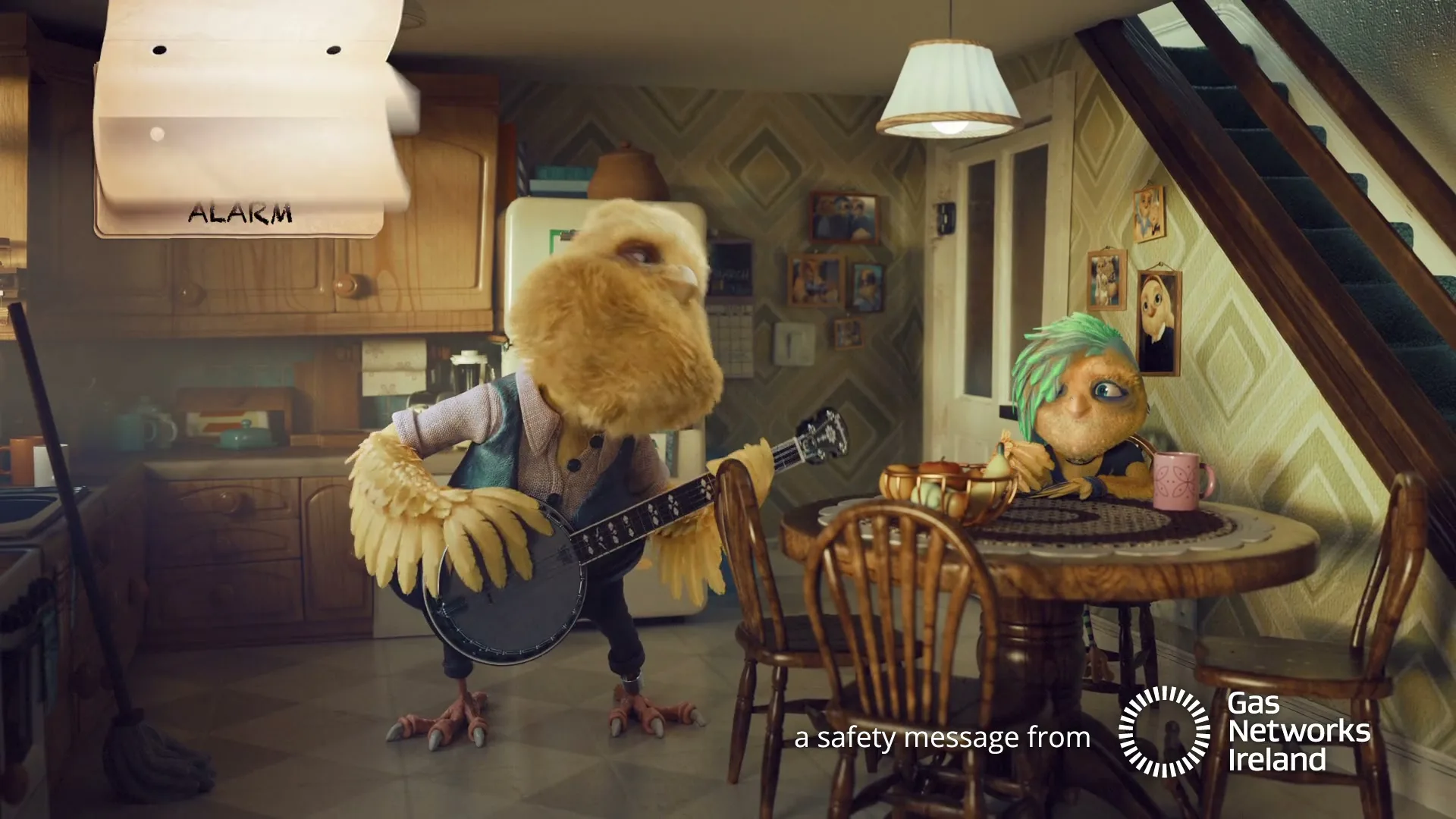 Two animated bird-like characters, one playing a banjo and the other sitting at a table, are in a kitchen with text on screen.