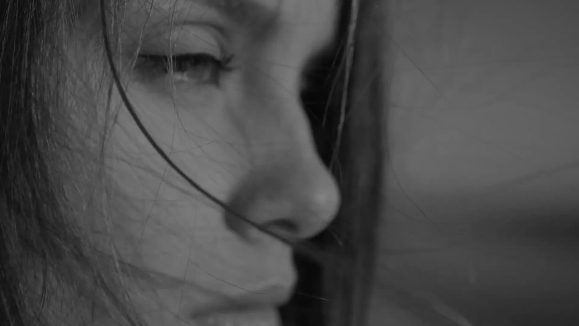 A woman's face in profile, with hair blowing in the wind, is superimposed over a man sitting on a beach, both in black and white.