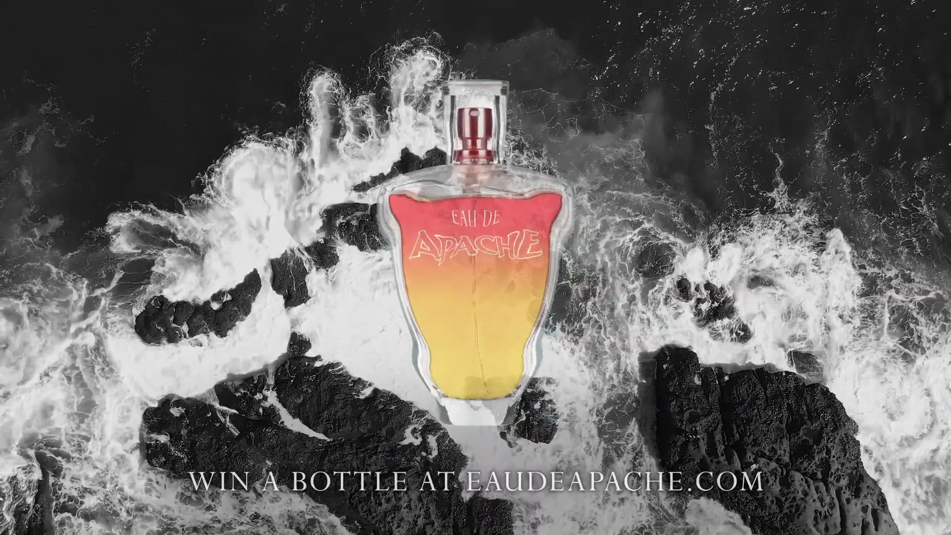 A perfume bottle with a red and yellow gradient is centered on a black and white background of crashing waves and rocks, with text below.