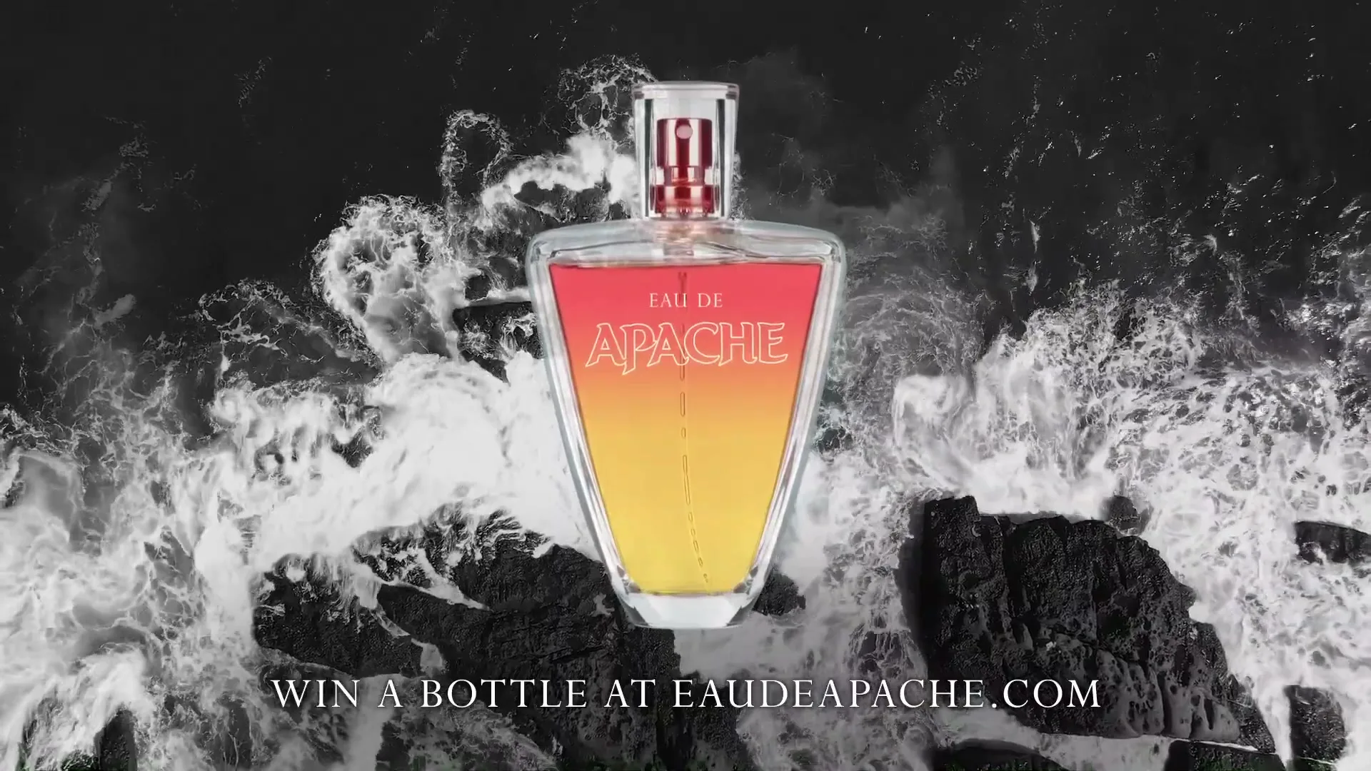 A perfume bottle with a red and yellow gradient is centered on a dark, rocky shore with white waves crashing around it, with text overlay.