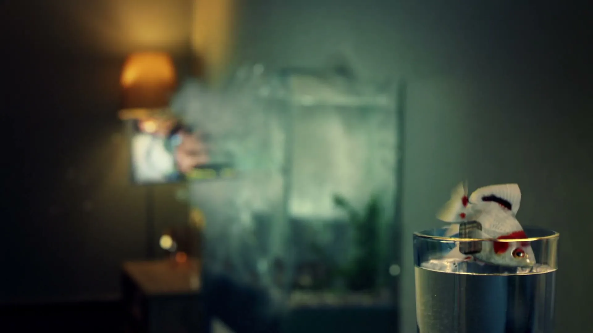 A goldfish with a guitar jumps out of a glass of water, then a fish tank explodes in a dimly lit room.