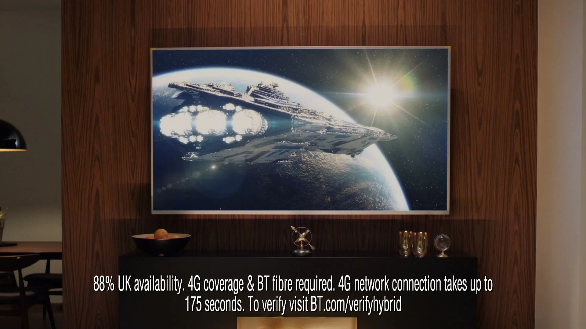 A large flat-screen TV displays a spaceship flying over a planet, with legal disclaimer text below, in a modern living room.