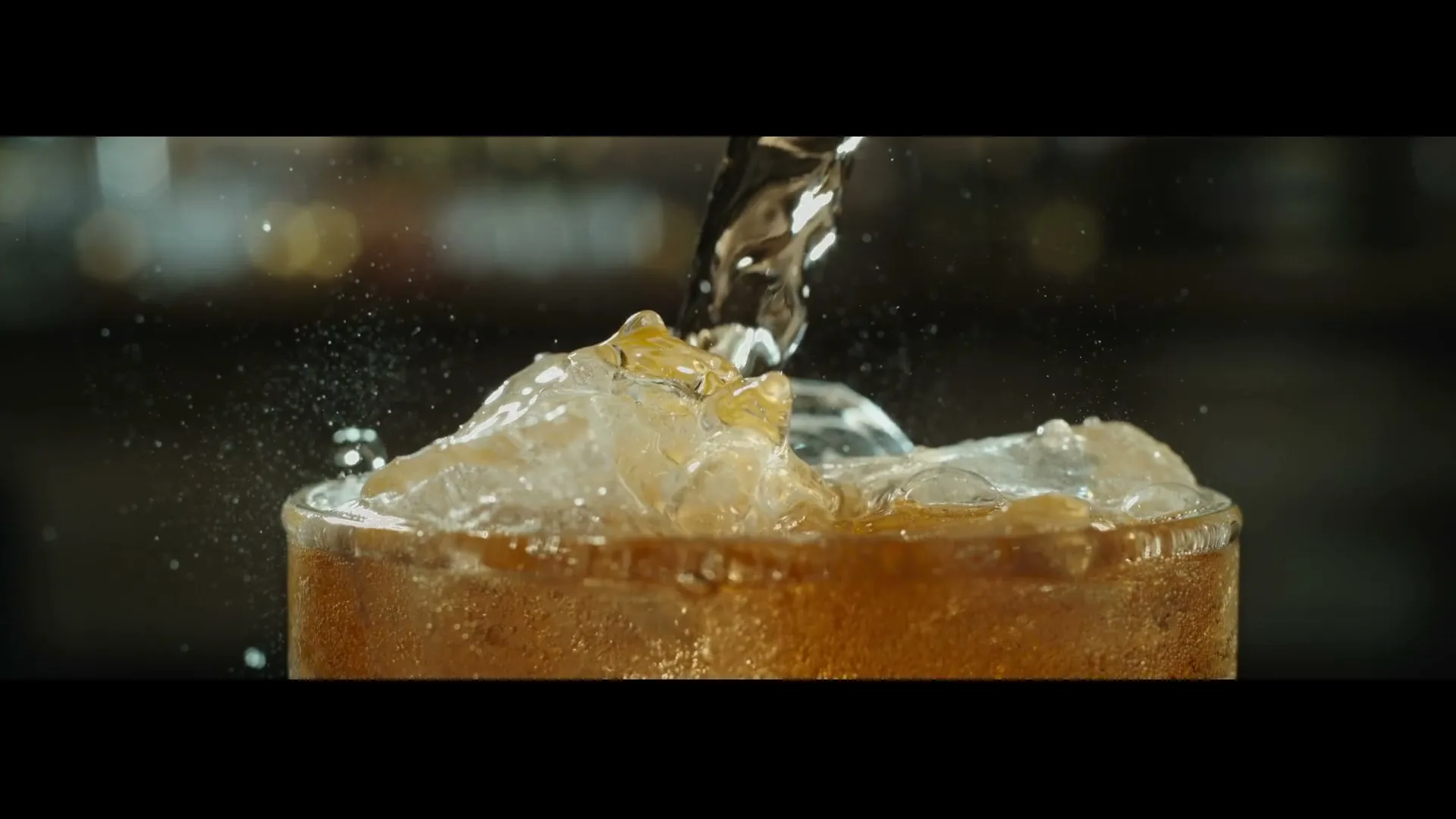 Cider is poured into a glass full of ice, creating splashes and bubbles, in a close-up shot.