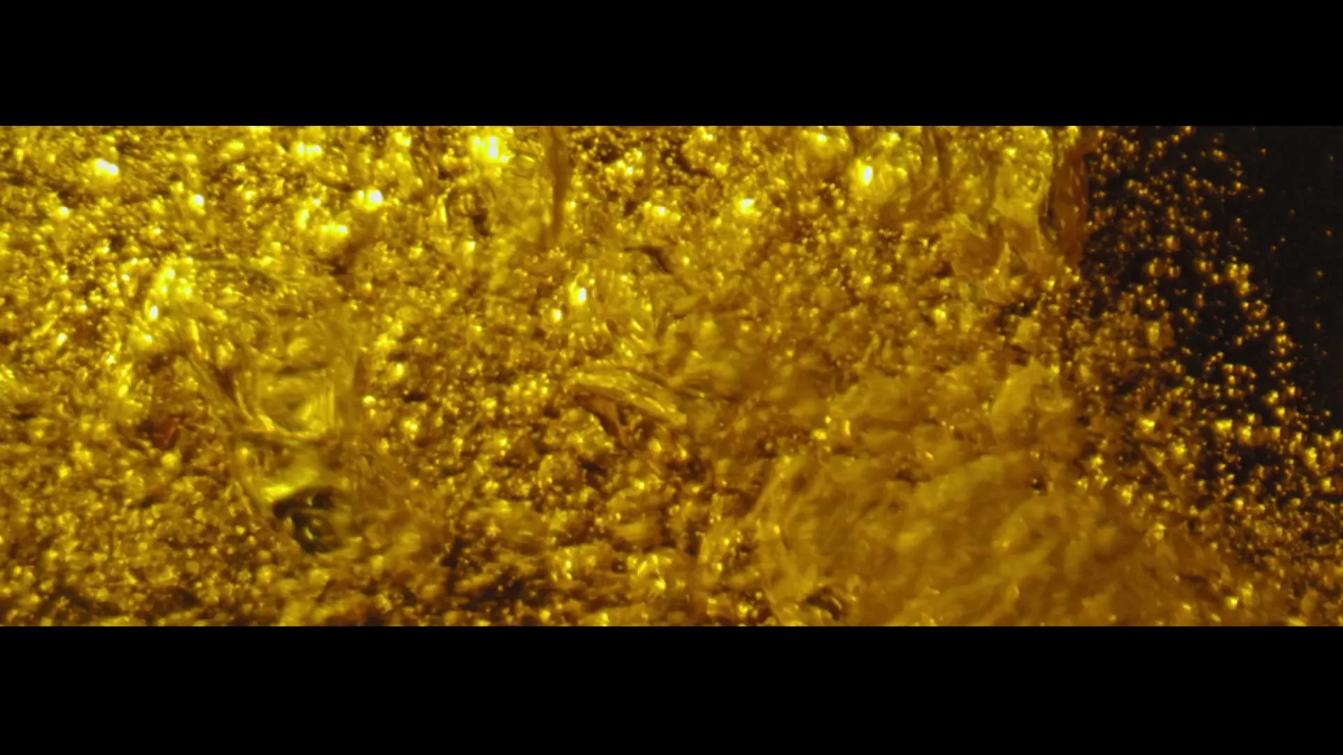 Golden liquid with many small bubbles fills the frame from left to right, creating a dynamic and effervescent visual.