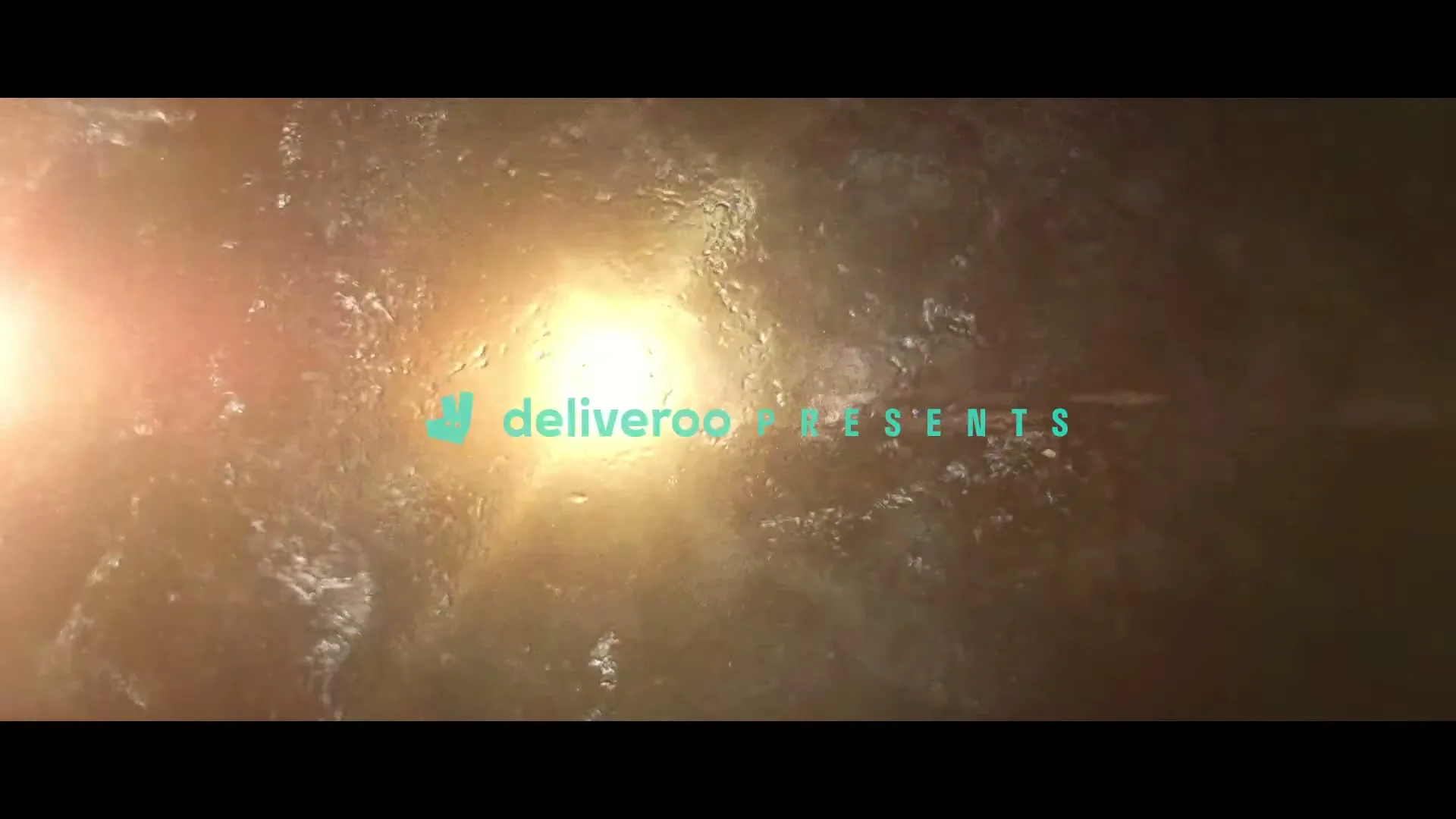 Dry spaghetti noodles are dropped into boiling water, creating a starburst effect with water droplets and bubbles, as the Deliveroo logo appears and disappears.