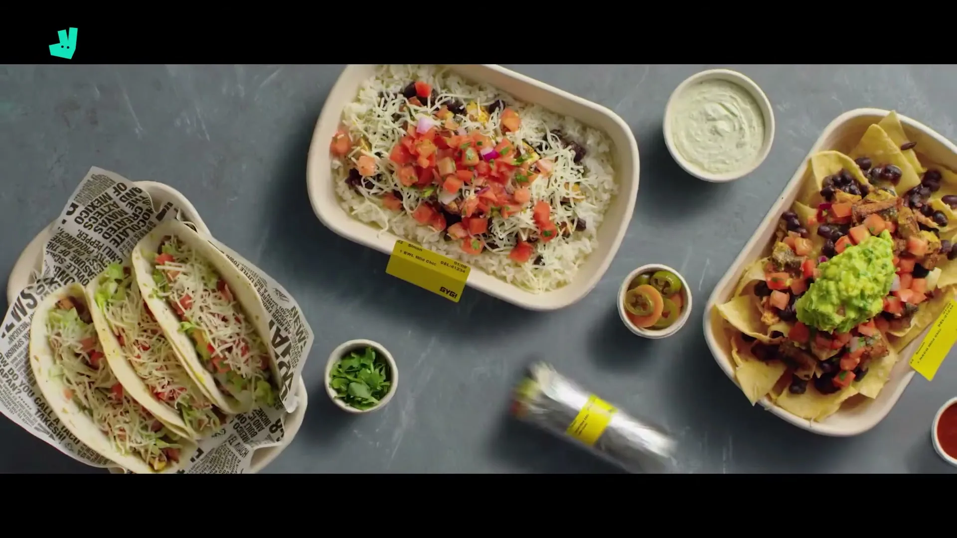 A top-down shot shows various Mexican dishes, including tacos, nachos, and a burrito, appearing on a grey surface.