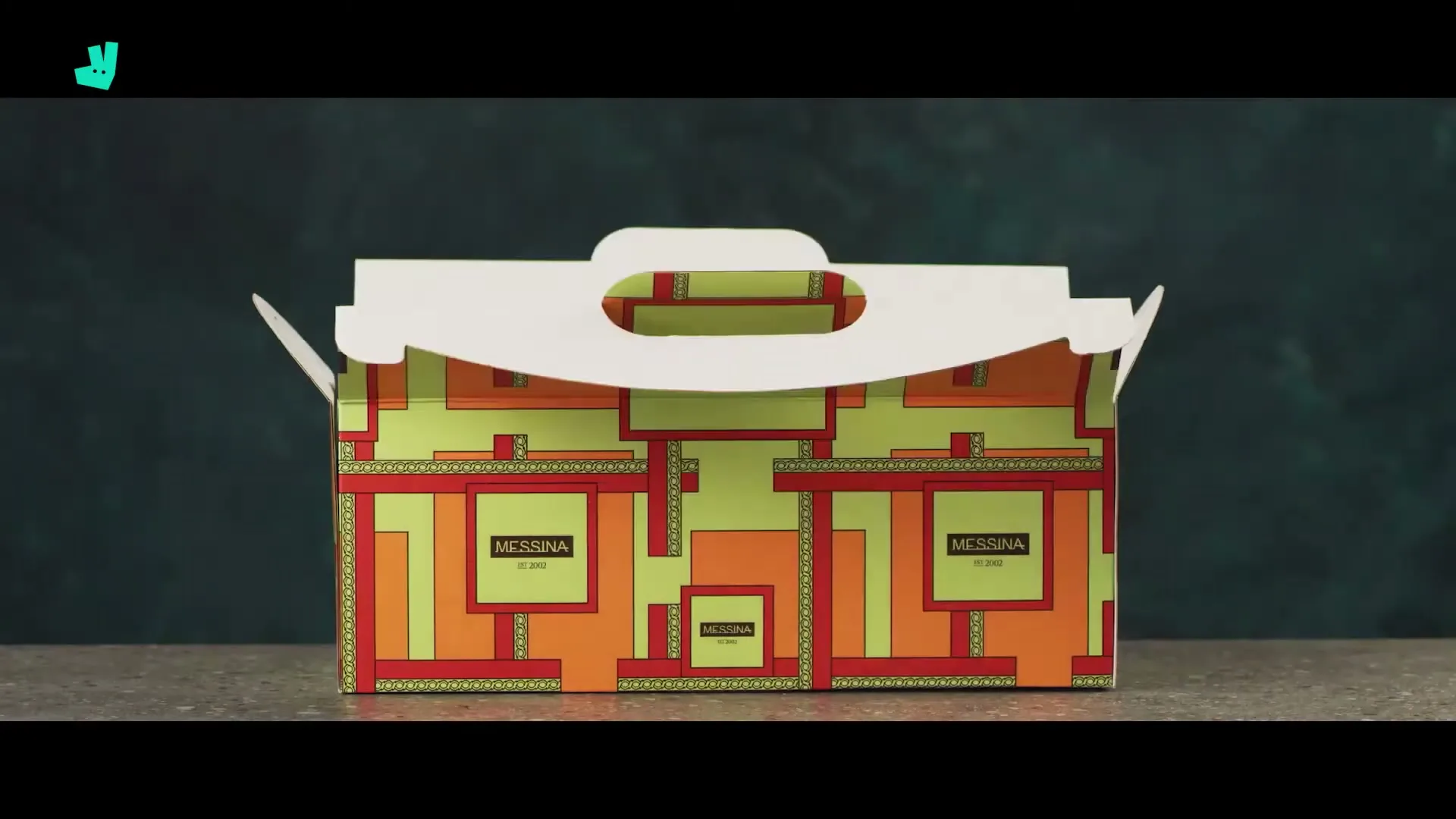 A female hand closes a colorful Messina gelato takeaway box on a grey countertop against a dark green wall.