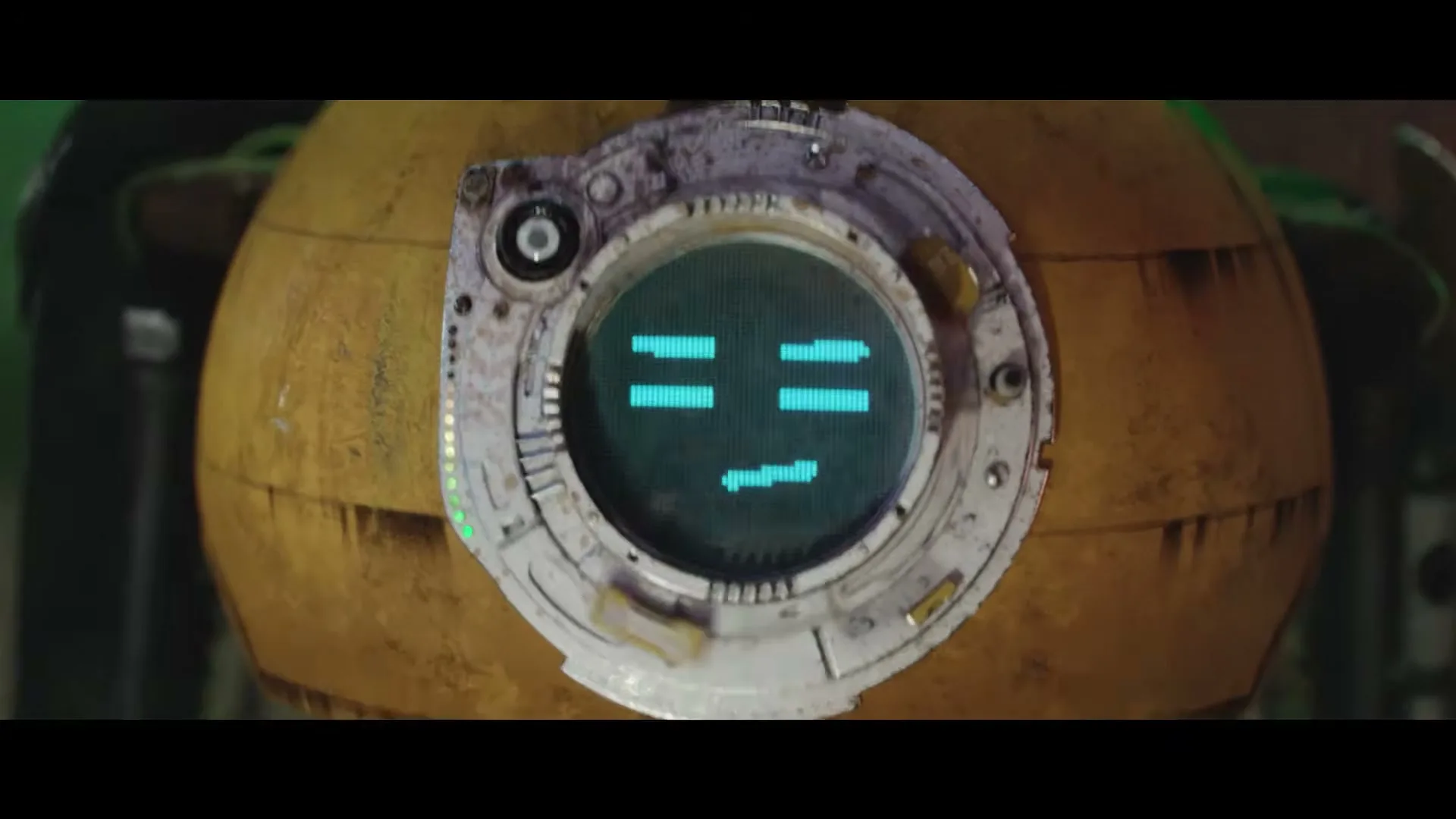 A yellow, spherical robot with a circular screen displaying a pixelated face is shown in a medium closeup.