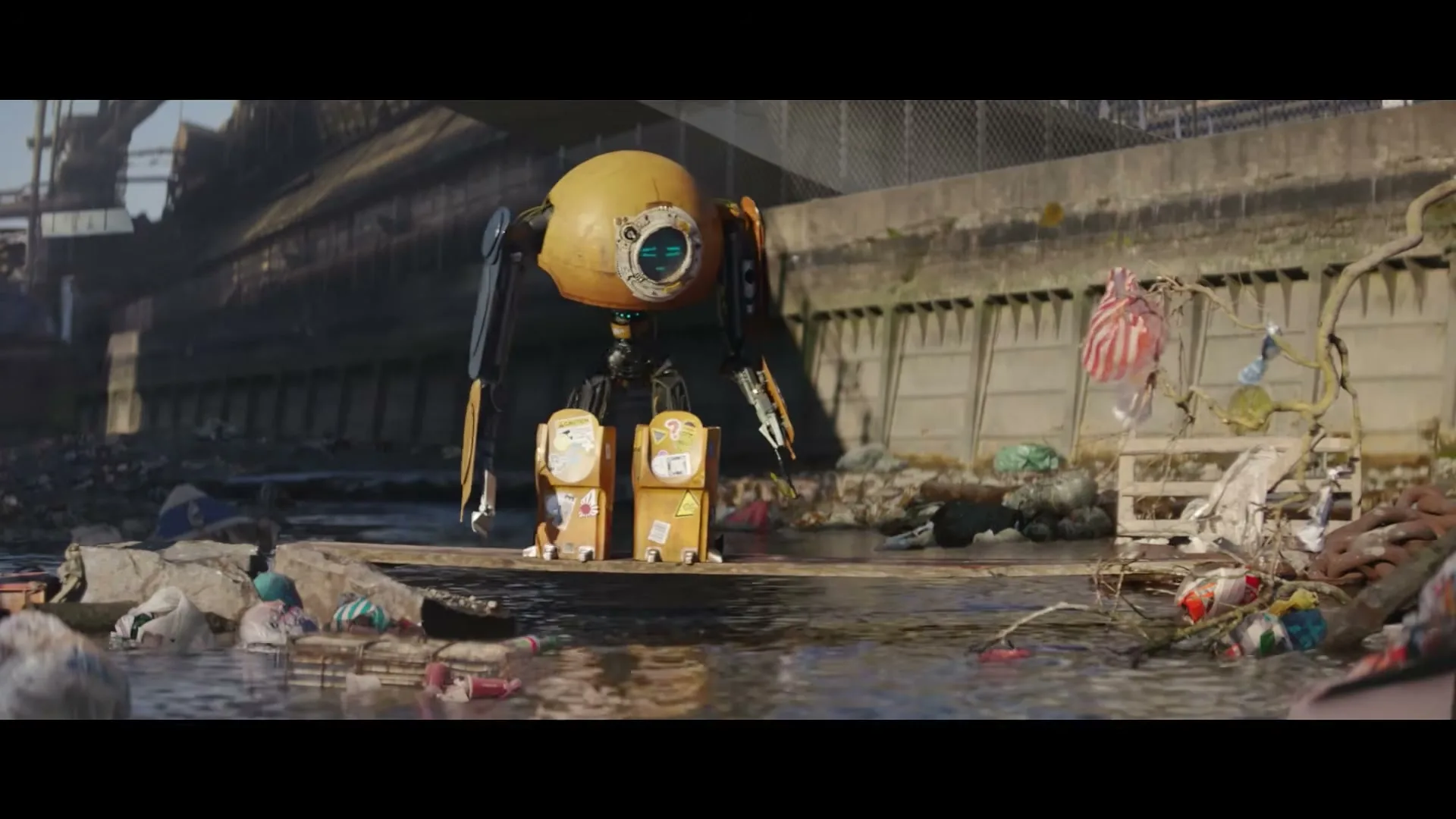 A yellow robot with a single eye and two box-like legs stands on a wooden plank over a polluted river, surrounded by trash and debris.