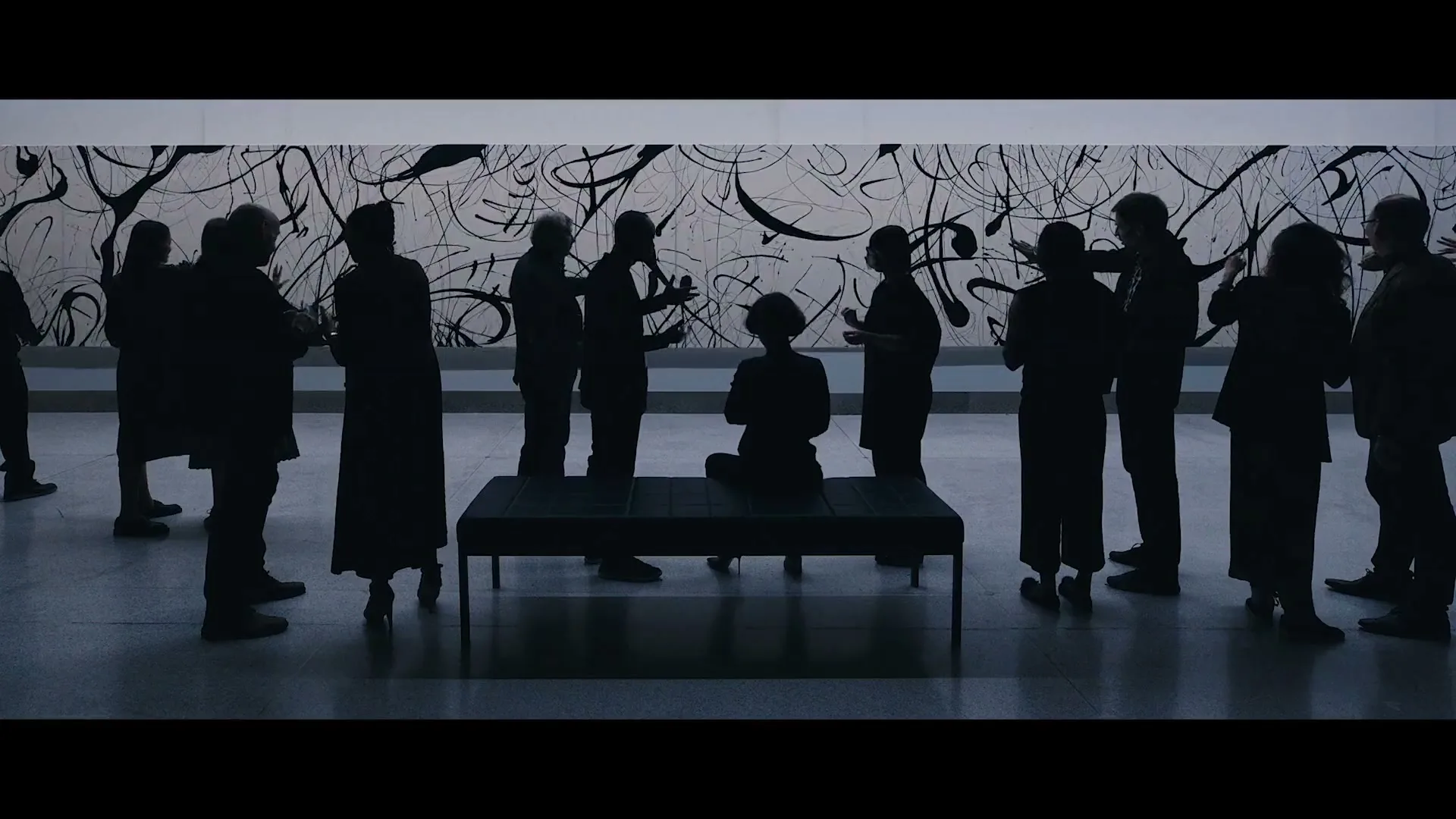 Silhouetted people stand and sit in a modern art gallery, looking at a large abstract painting on the wall.