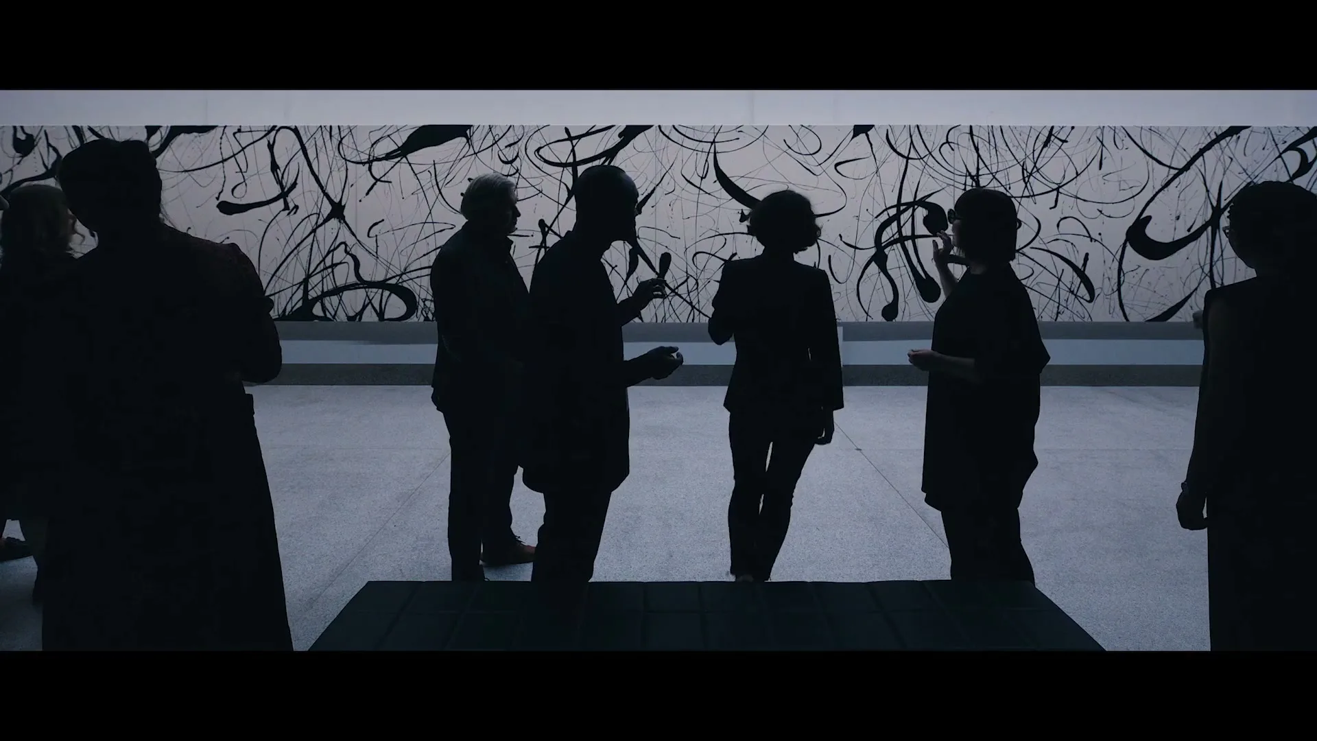 Silhouetted people stand and converse in an art gallery, admiring a large abstract painting on the wall.