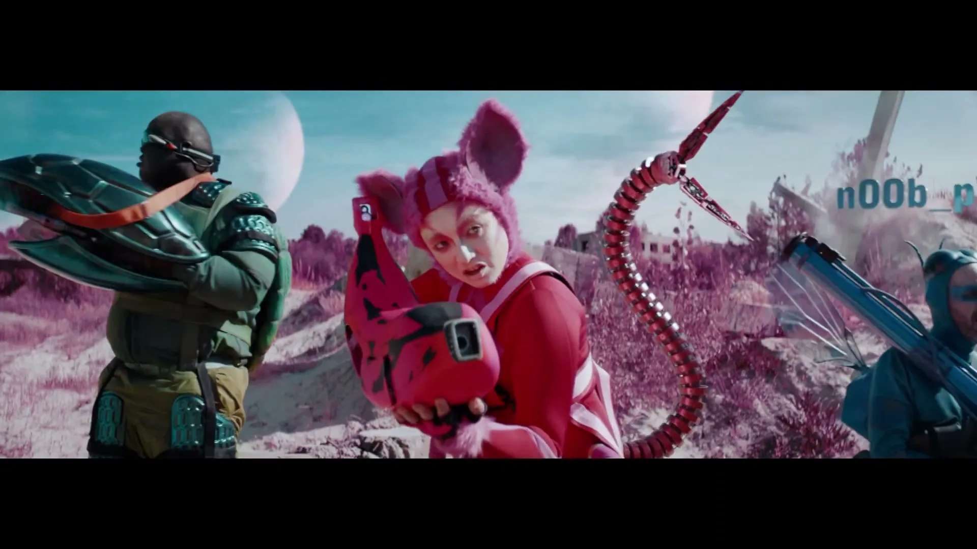 A person in a pink mouse costume holds a device, flanked by two other people in futuristic gear on a surreal, alien landscape.