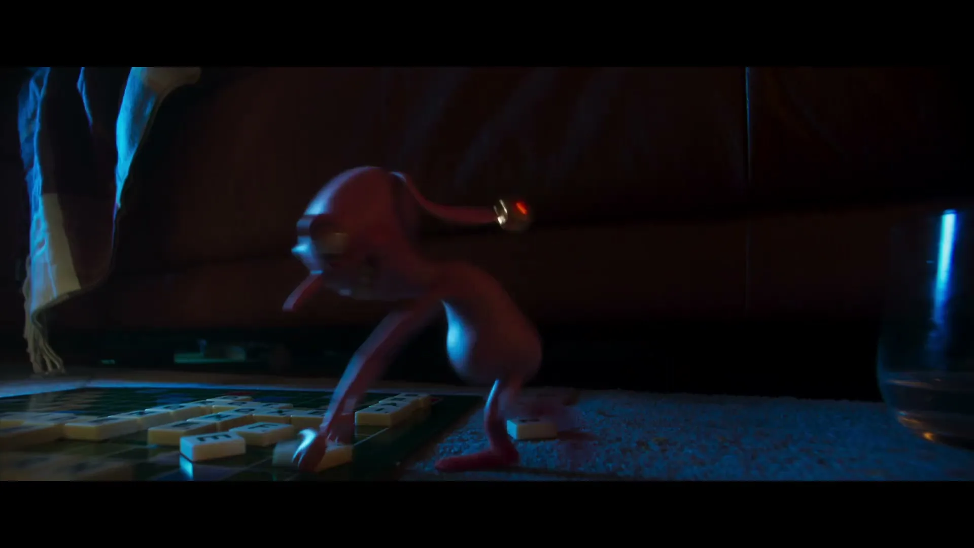 A mischievous pink animated creature with a top hat and bells dances on a rug next to a Scrabble board in a dimly lit living room.