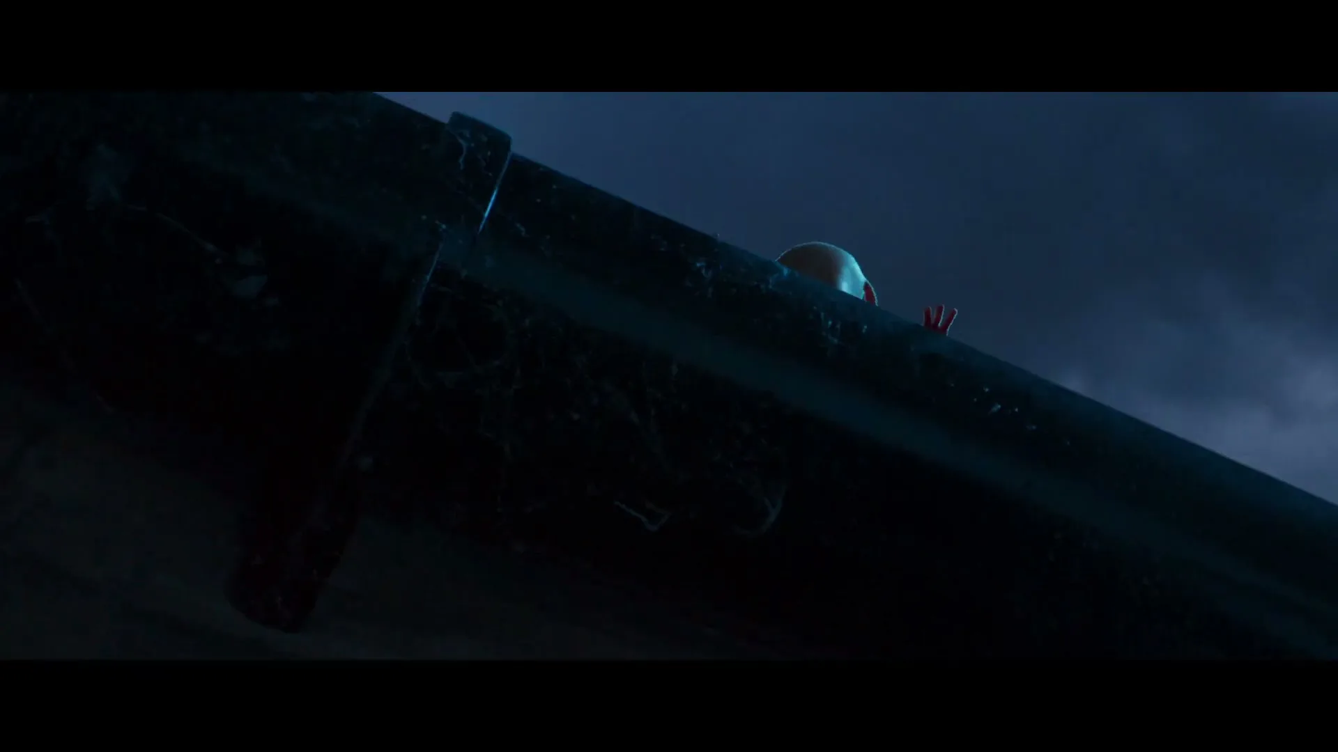 A small, bald, pink creature with red clothing struggles to climb over a dark gutter against a dark blue, cloudy sky at night.
