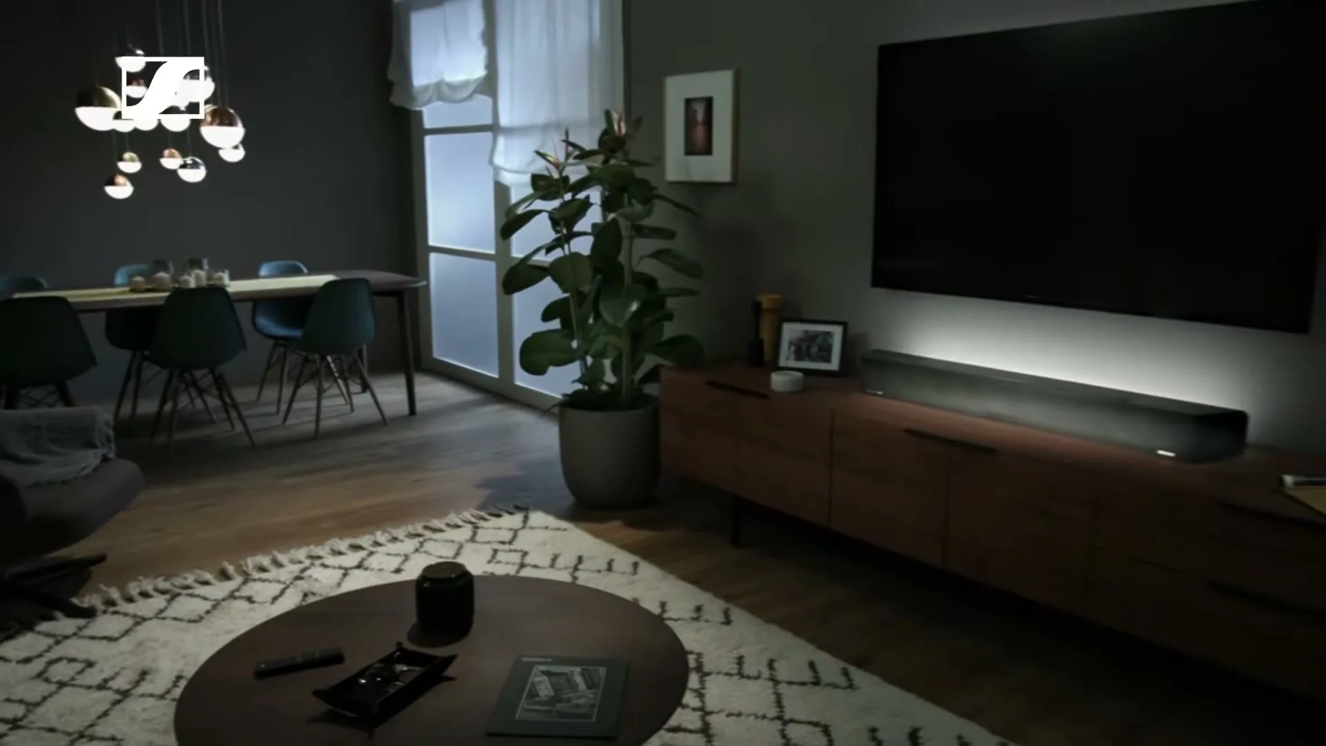 A wide shot of a modern living room with a dining area, featuring a soundbar under a large TV, and a potted plant.