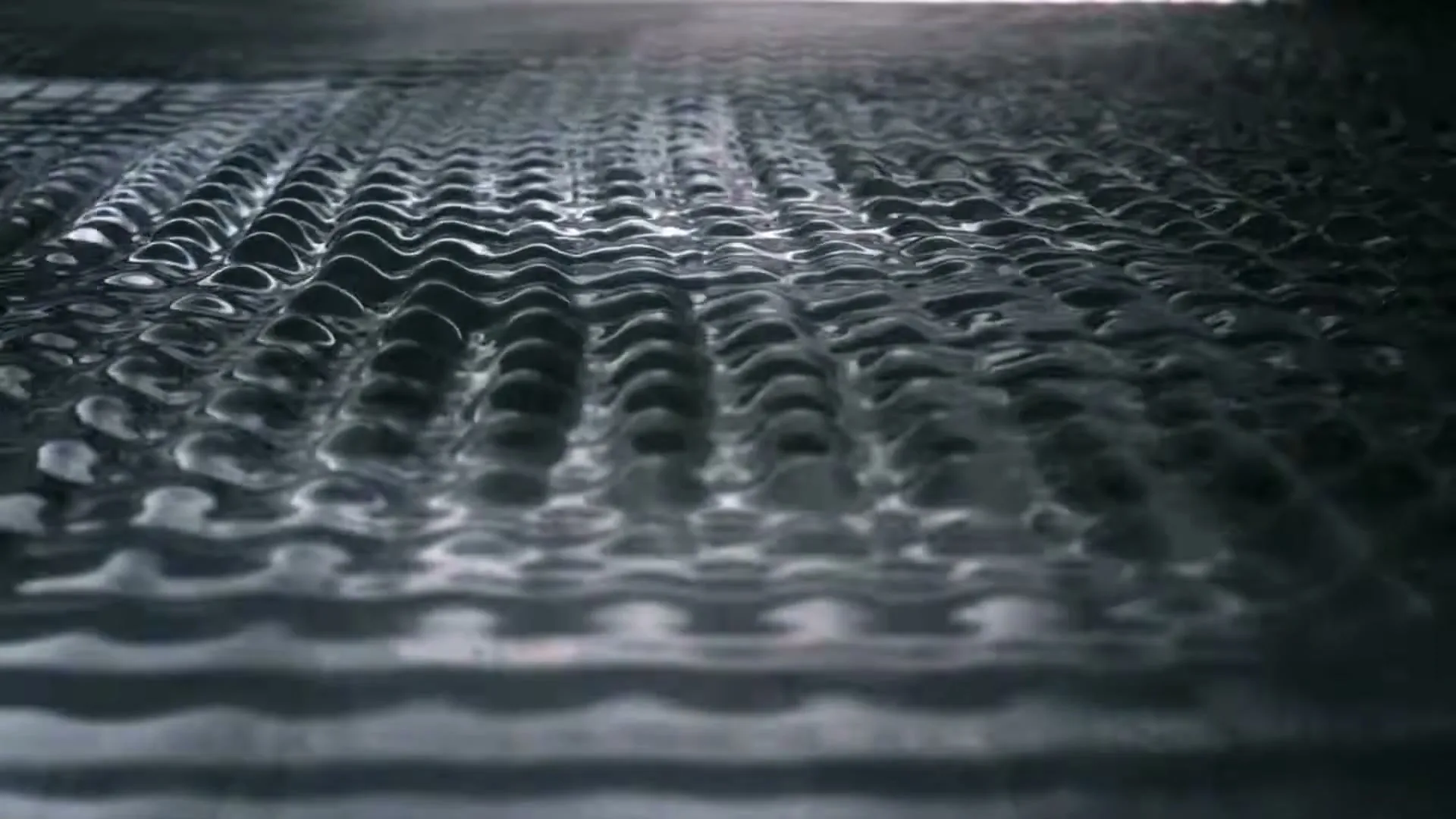 Water ripples on a dark, reflective surface, creating a mesmerizing pattern of waves and light reflections.