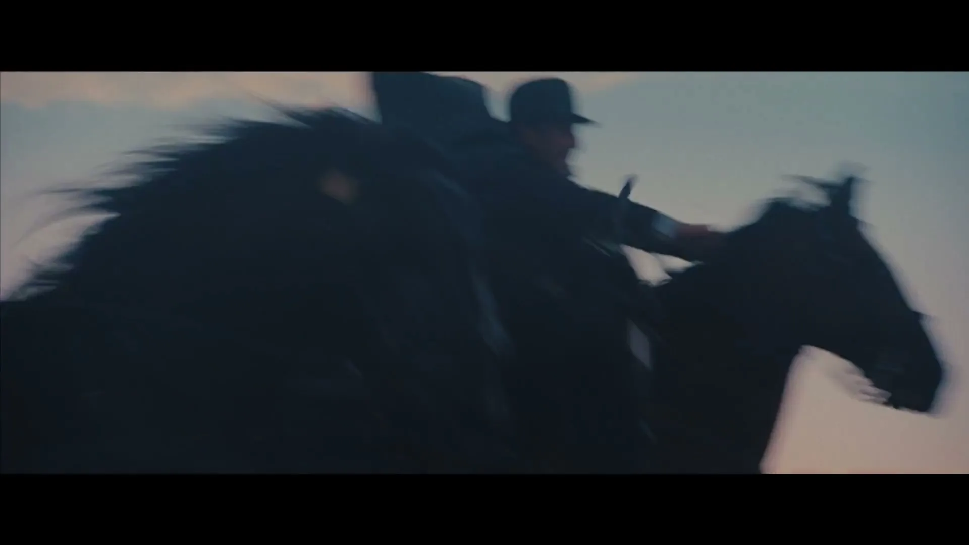 A man in a hat rides a horse at high speed, silhouetted against a pale sky, moving from left to right.