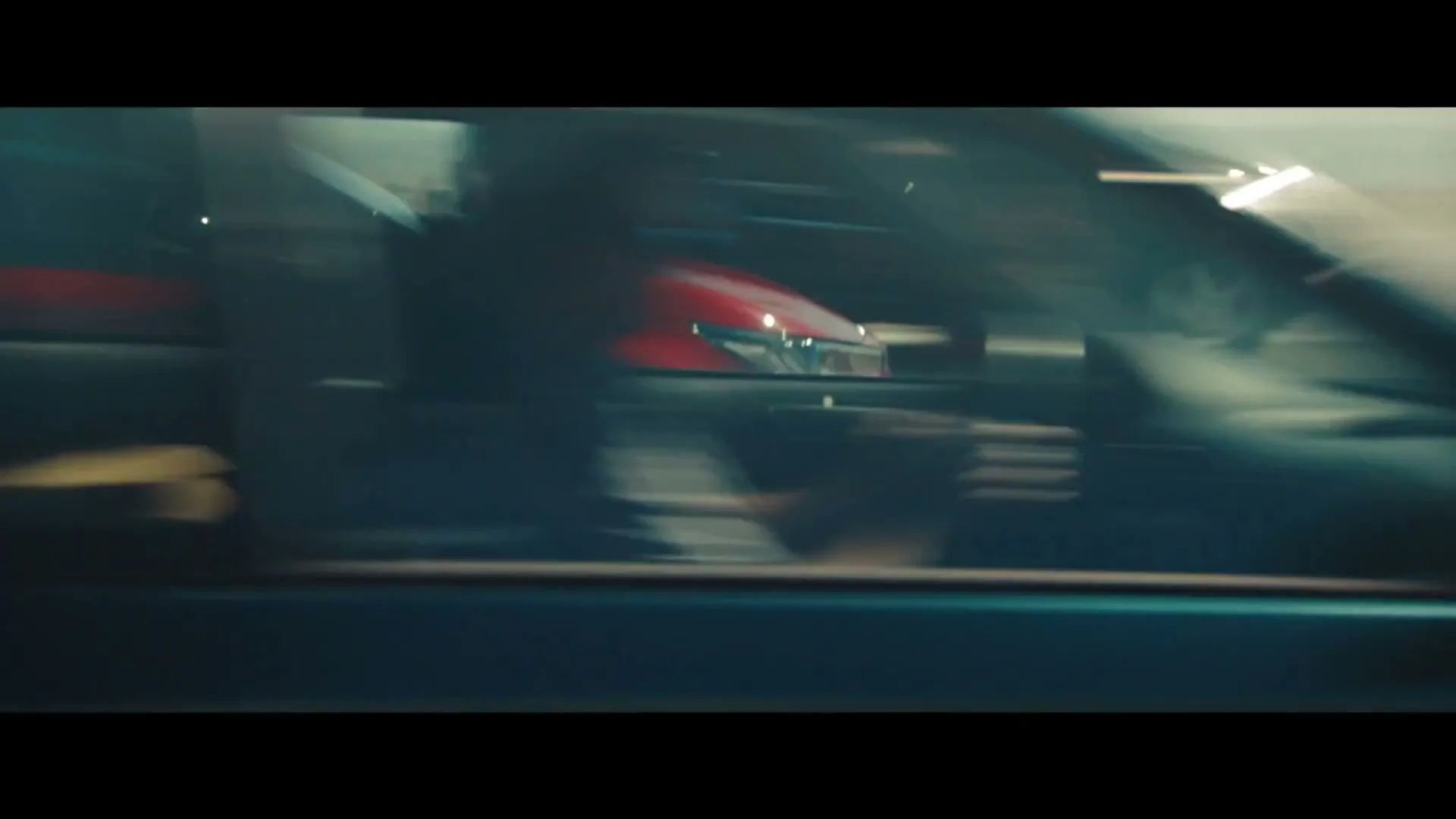 A red Toyota Hybrid car drives on a highway, with other cars blurred in the background, under a bright sky.