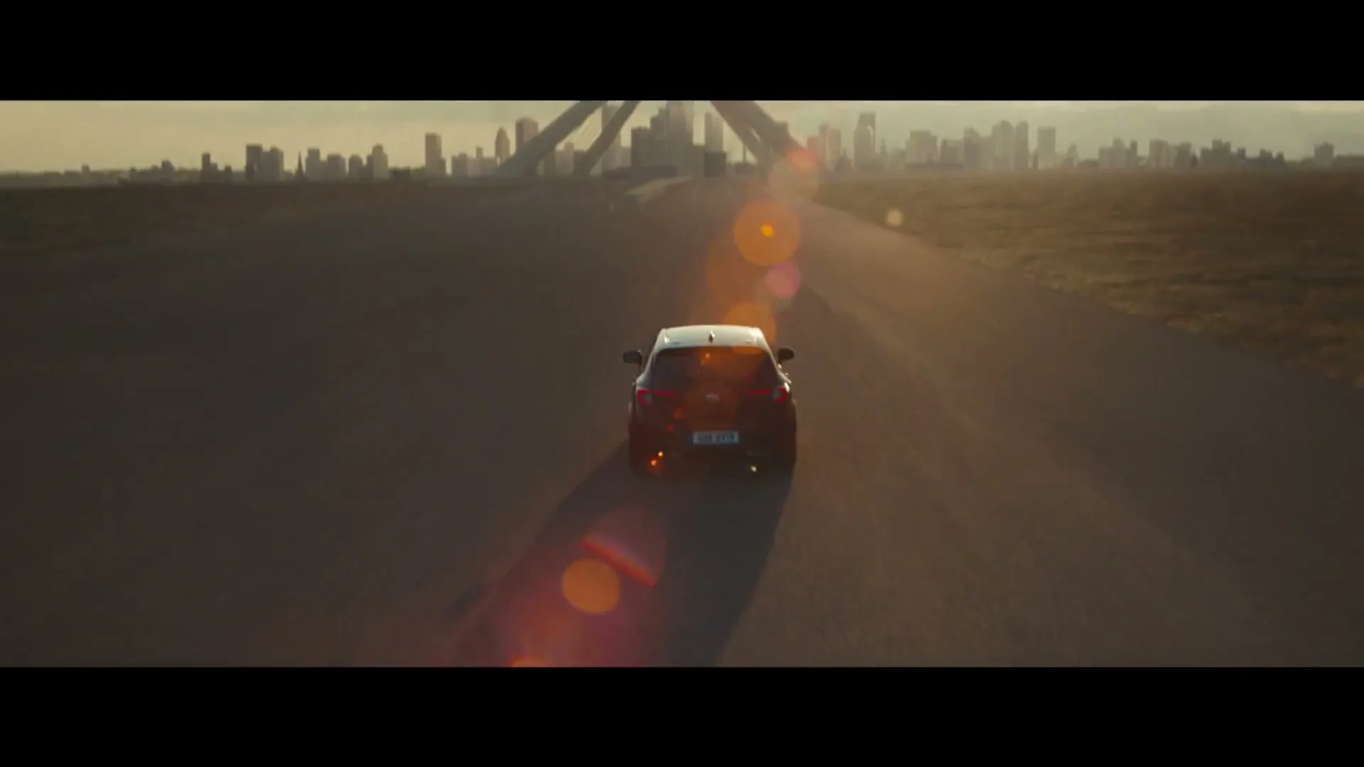 A black Toyota car drives away from the camera on a wide, empty road towards a futuristic city skyline at golden hour.