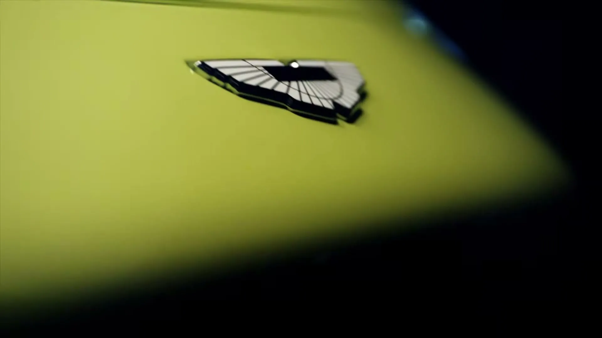 The Aston Martin logo is seen in a macro detail shot on a lime green car, with a dark background.