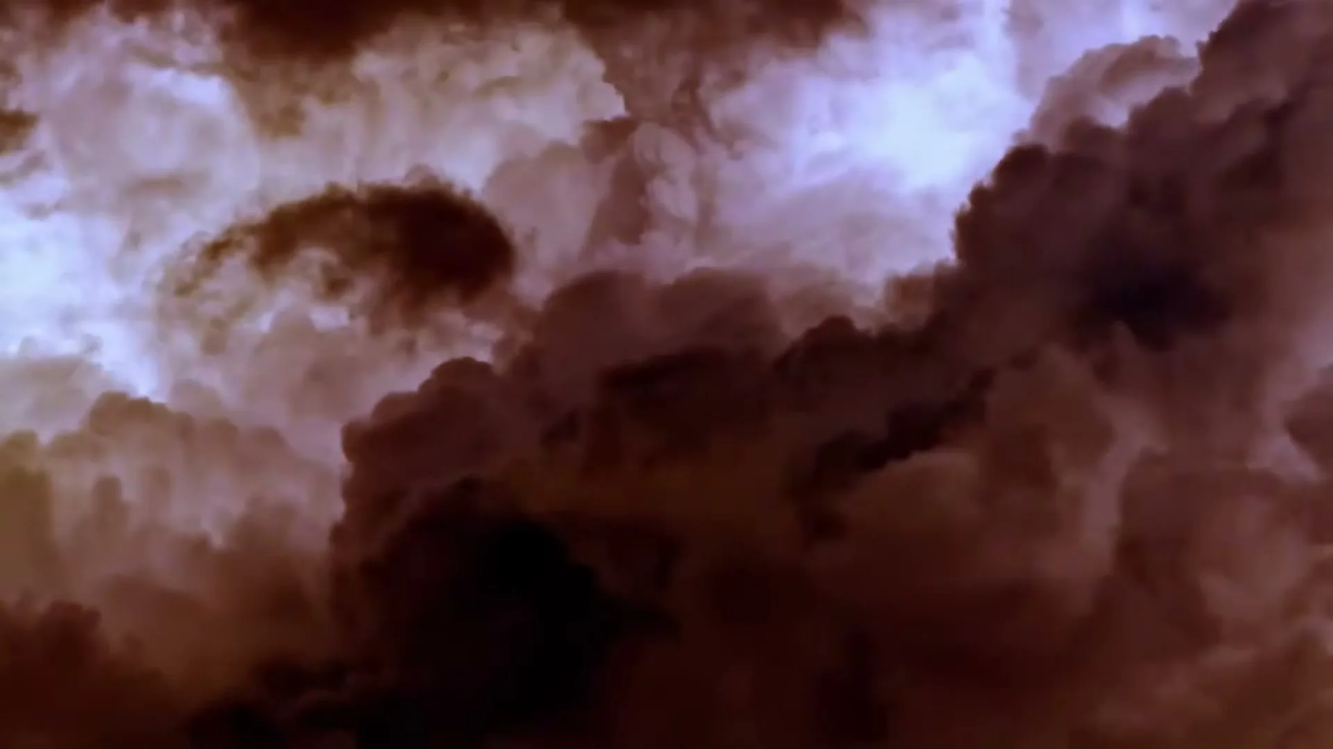 Dark, ominous clouds swirl and billow across the sky, with hints of light breaking through the dense formations.