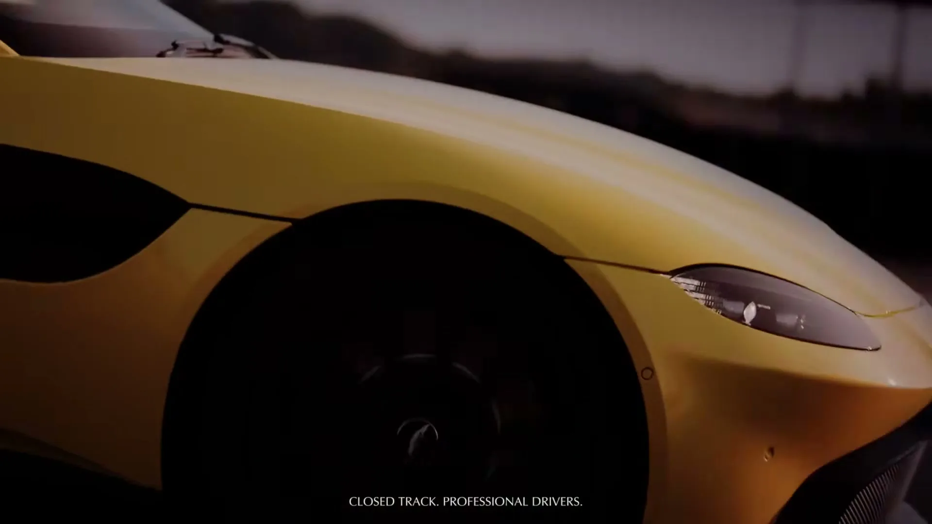 A close-up shot of a yellow Aston Martin sports car, with its sleek design and dark wheels, as it drives on a track.