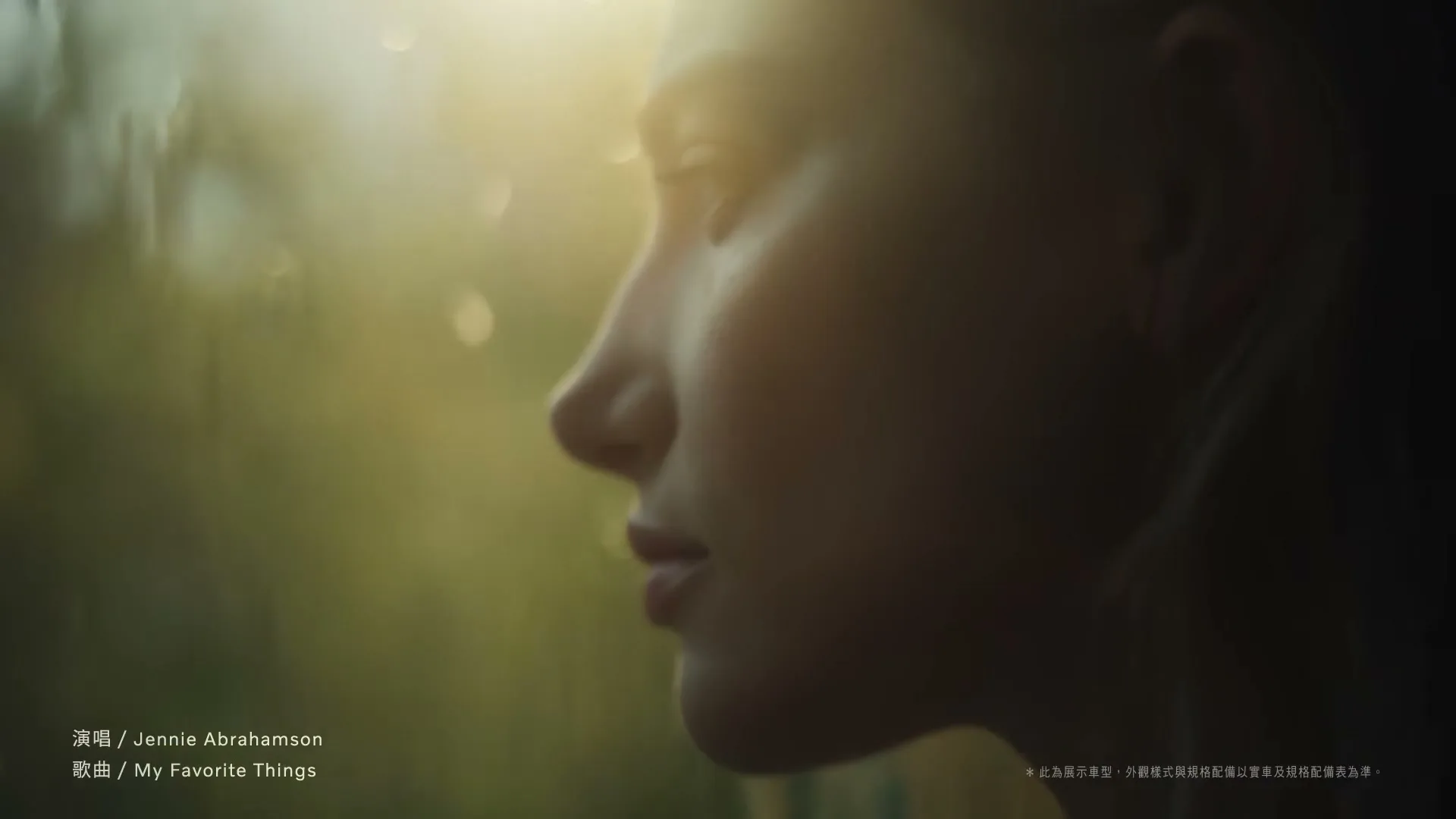 A young woman with light skin and dark hair looks out a window, with soft light on her face, in a car.