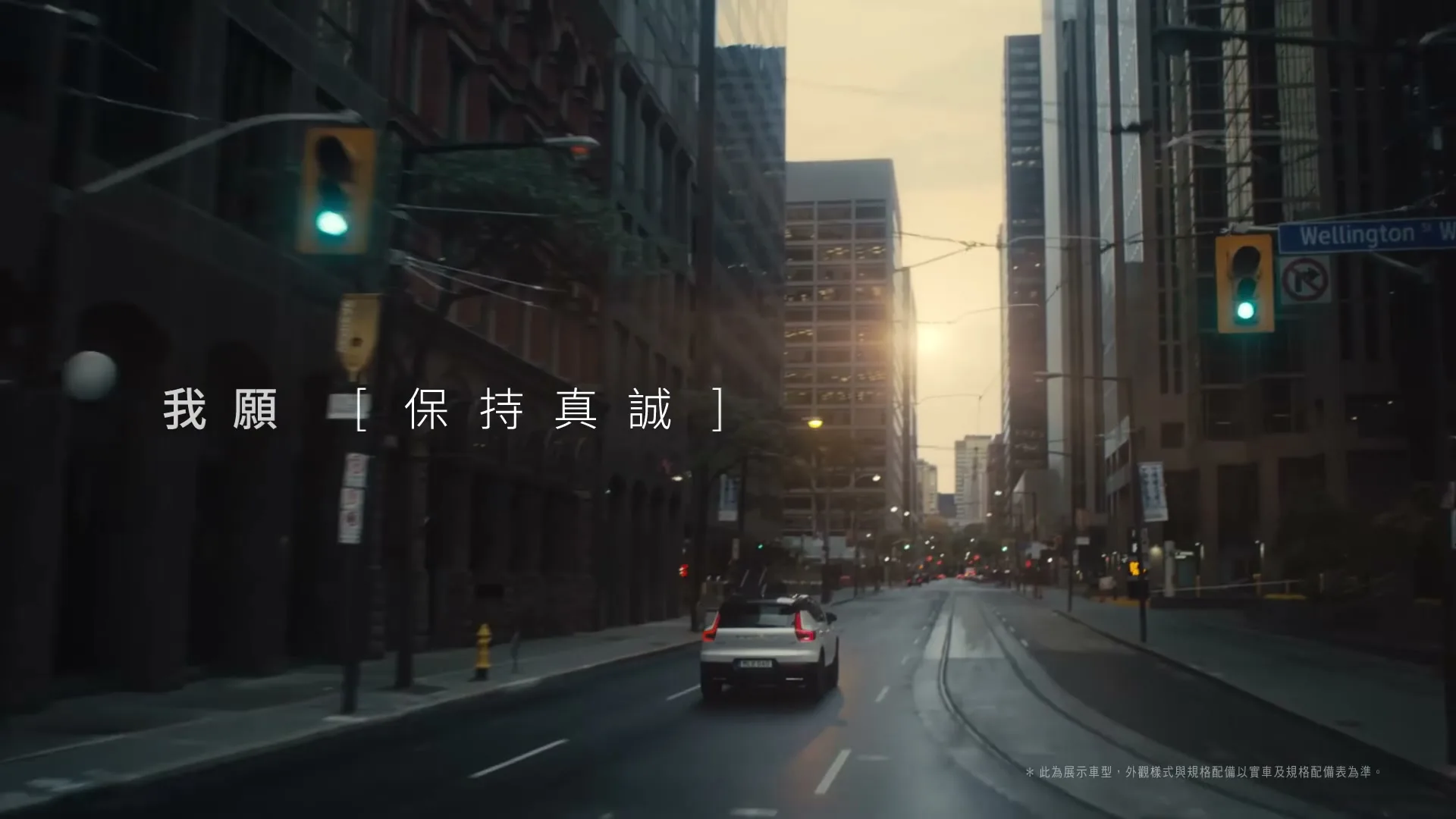 A white Volvo car drives away from the camera down a wet city street lined with tall buildings at sunset, with Chinese text on screen.