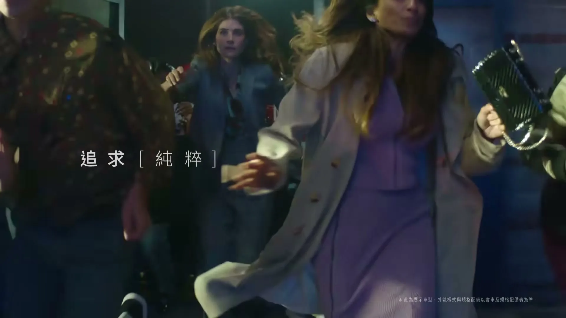 A diverse group of young adults, including a woman in a purple dress and trench coat, run through a dark, urban interior space at night.