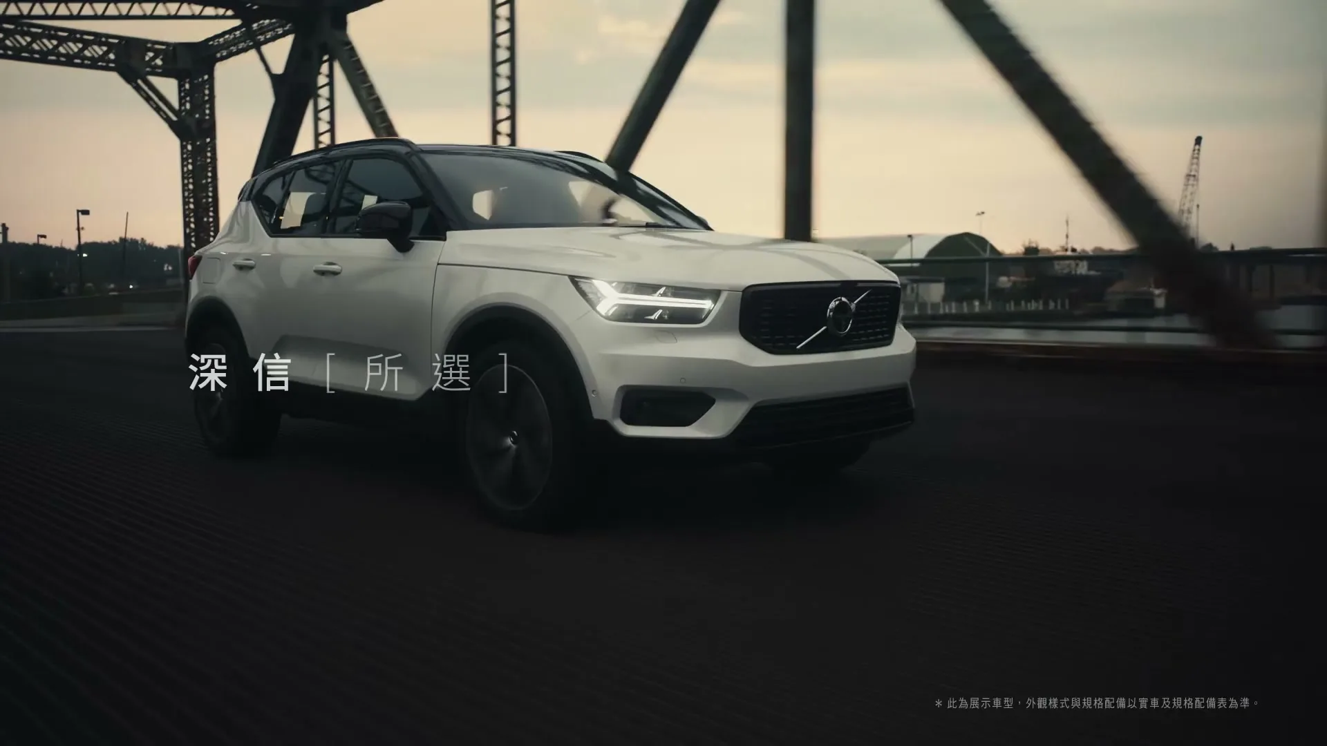 A white Volvo XC40 drives across a bridge at dusk, with text appearing on screen.