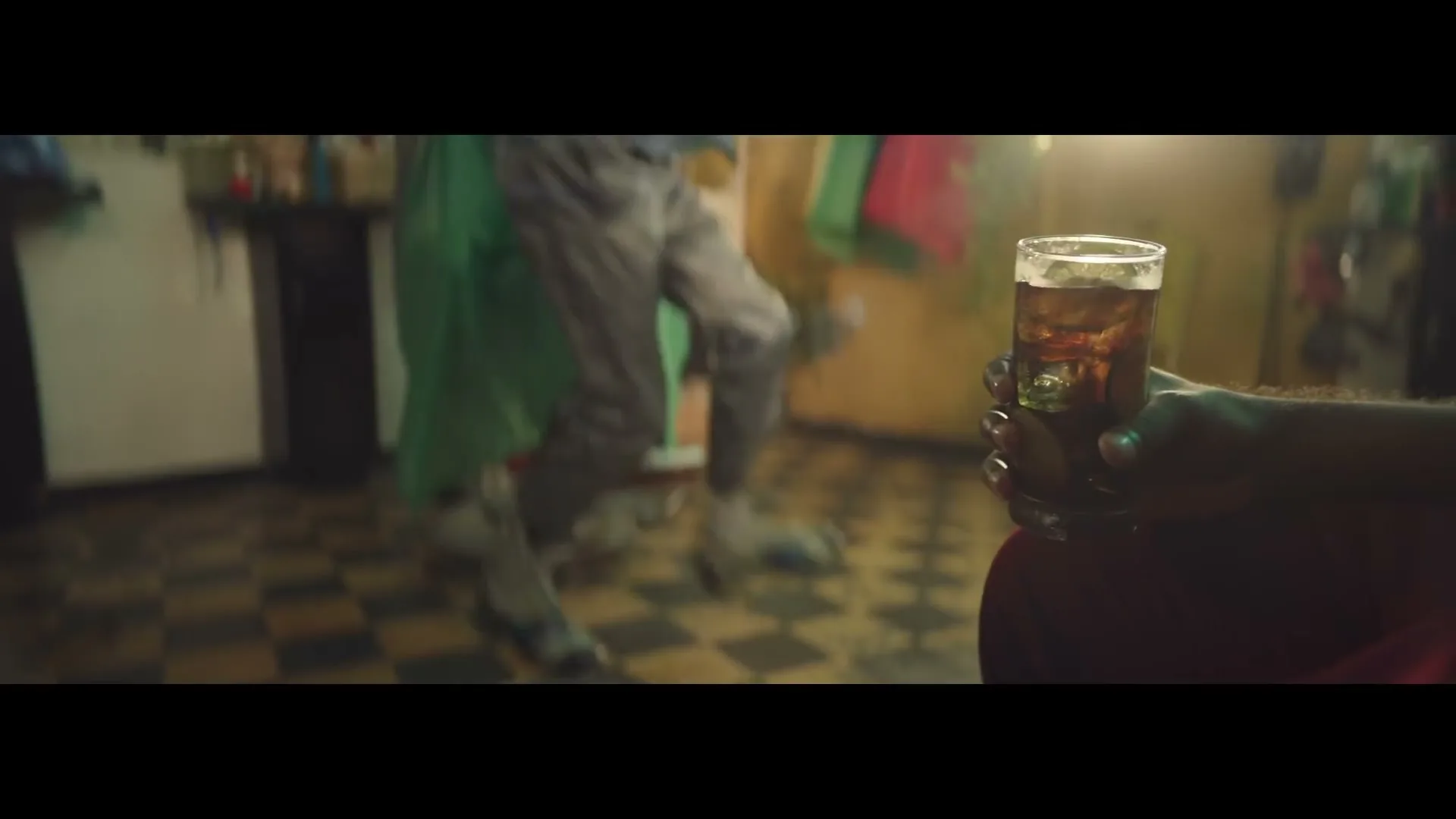 A person holds a glass of Bacardi and coke while another person dances in the background of a barbershop.