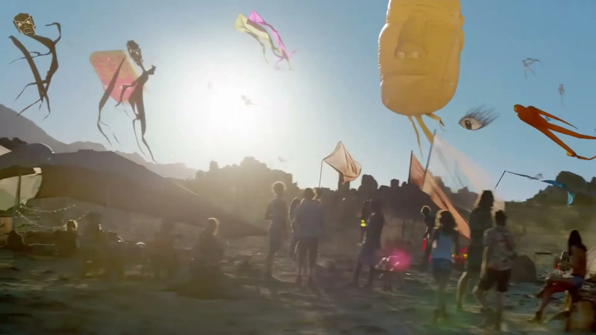 A diverse group of young adults gather in a desert landscape, surrounded by large, colorful, abstract kites flying high in the bright blue sky.