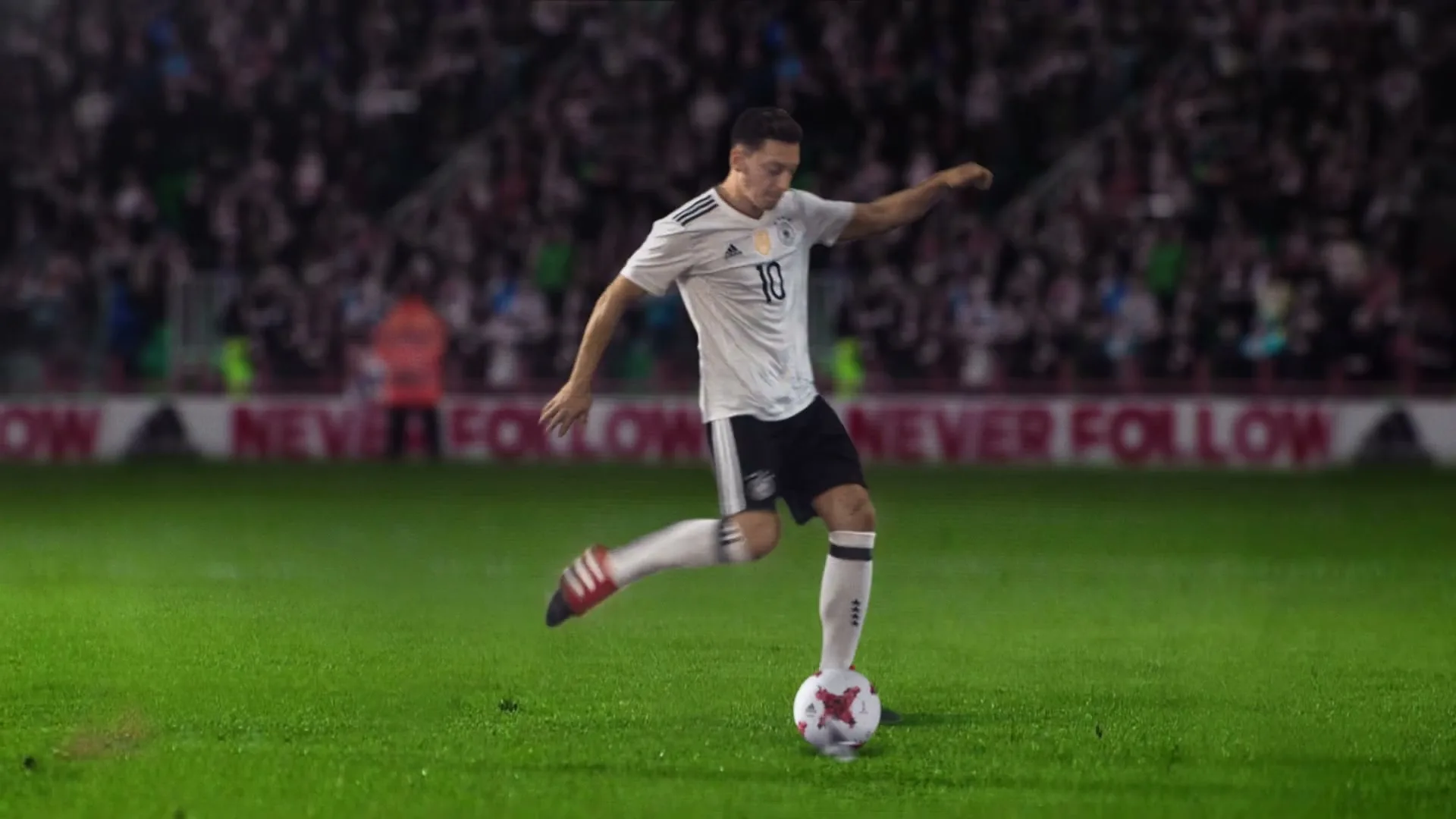 A male soccer player in a white jersey kicks a soccer ball on a green field in a stadium at night.