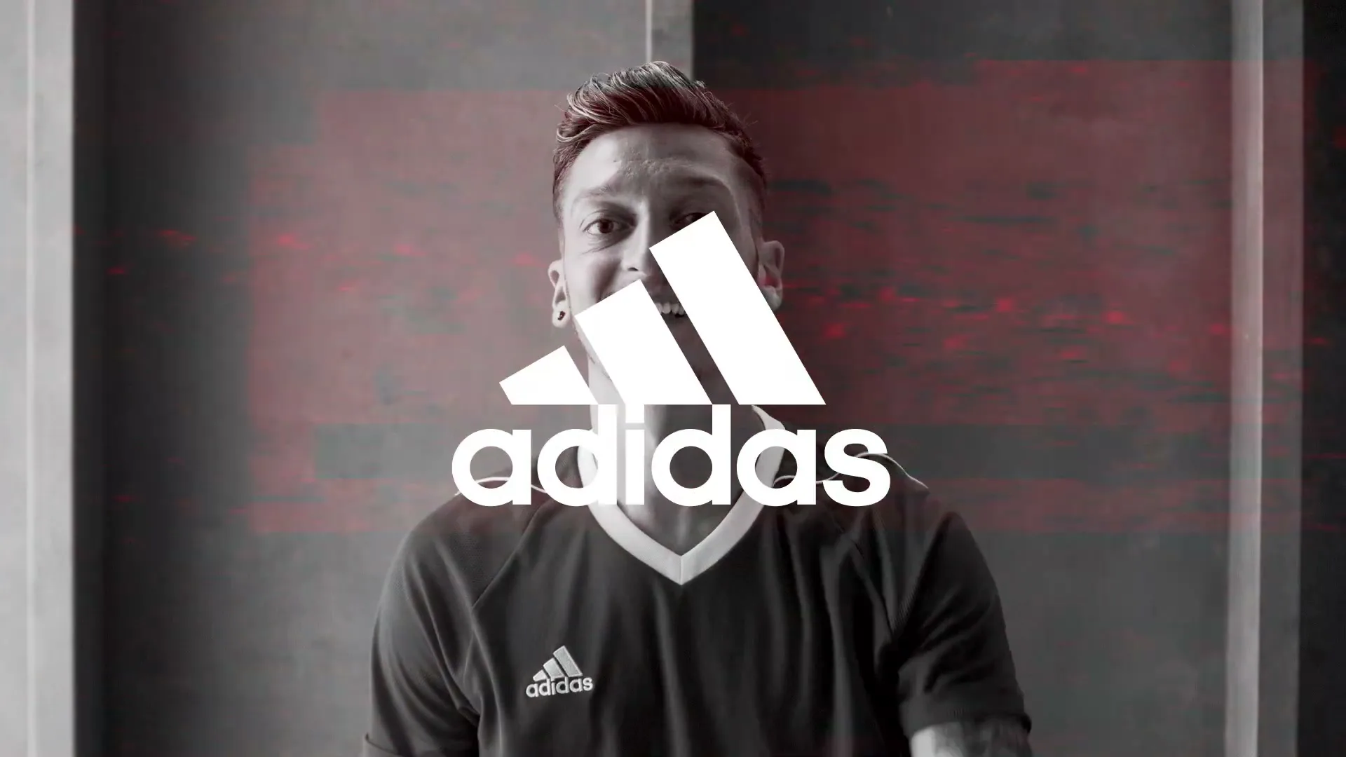 Mesut Özil, a male soccer player in his 20s, points at the camera in a room with a red wall, then the Adidas logo appears.